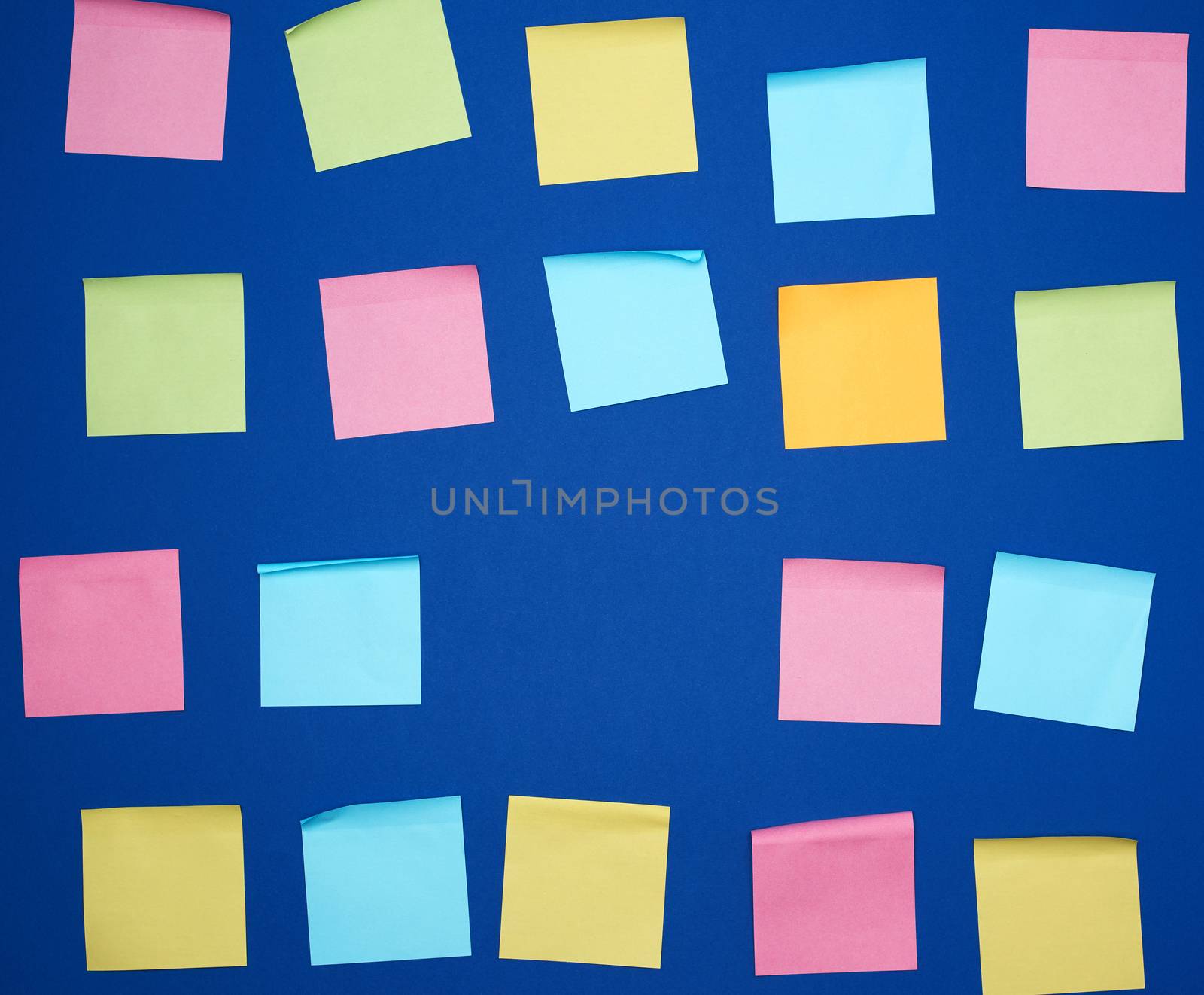 many glued square multi-colored blank stickers on a blue background, close up
