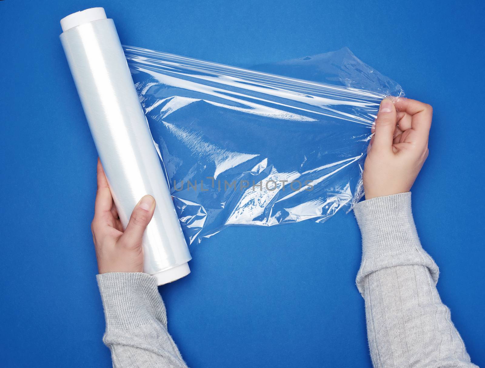 hand hold a large roll of wound white transparent film for wrapping food, top view, blue background 