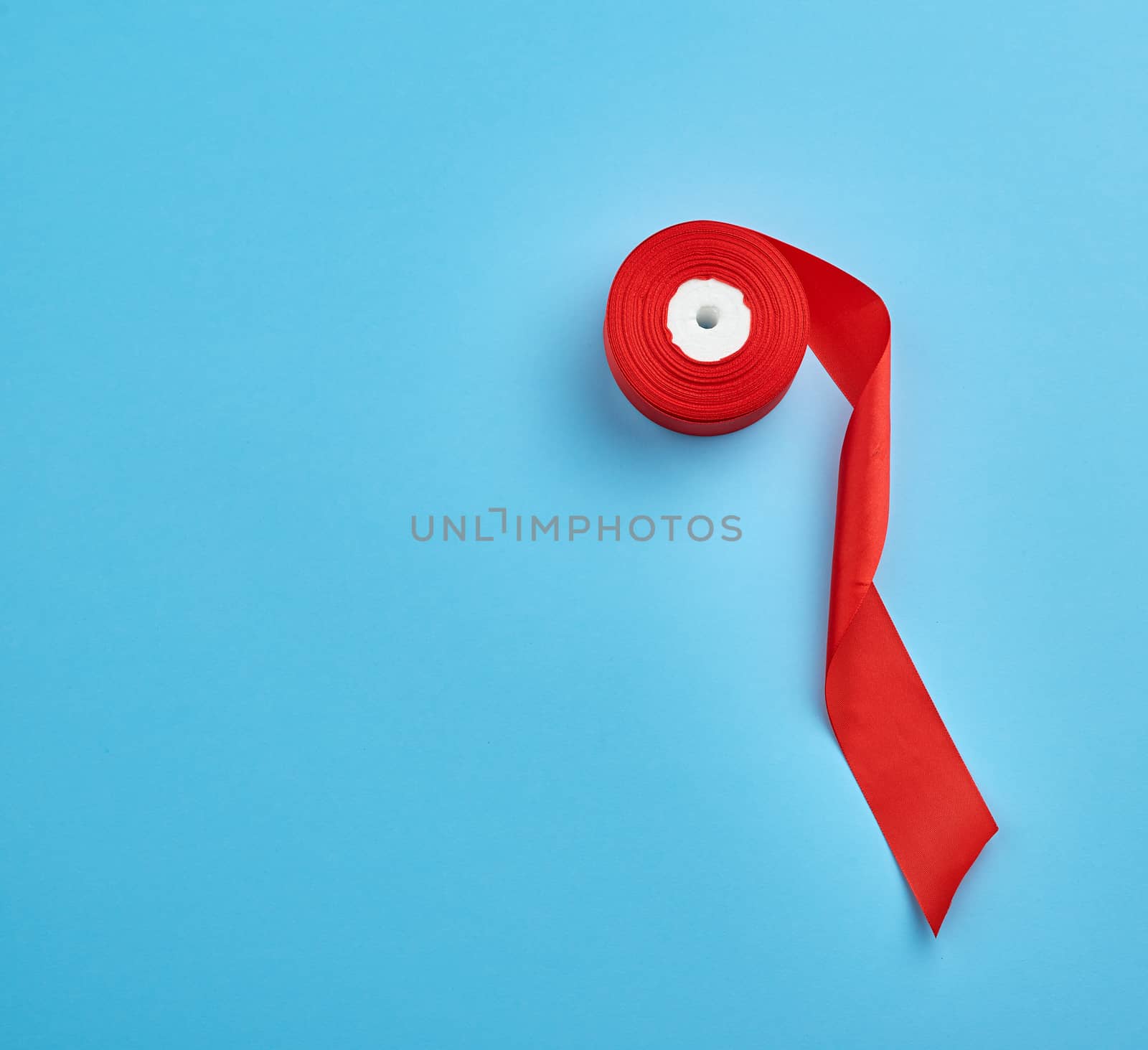 spools with red satin ribbon on a blue background, top view