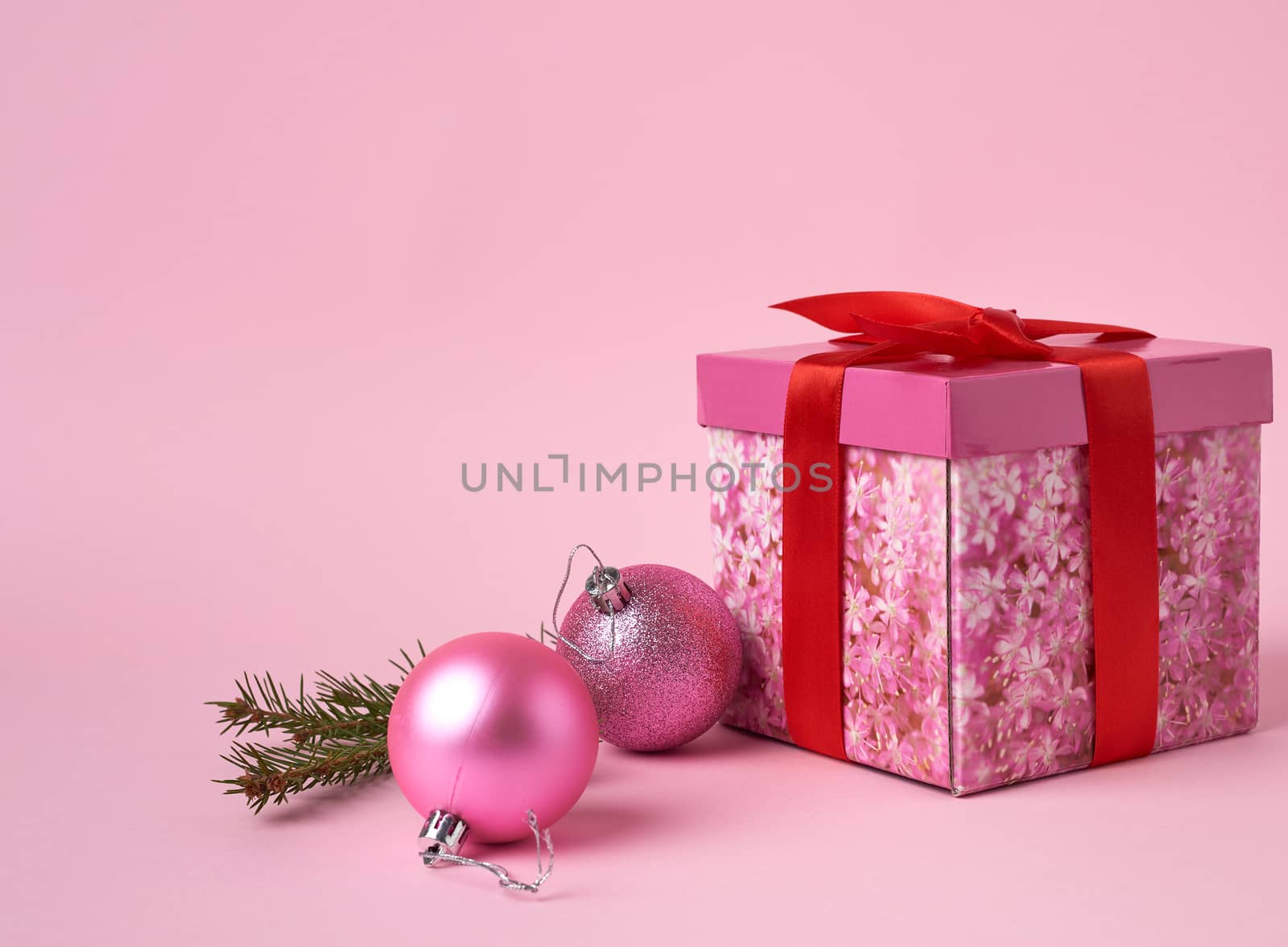 pink gift box with bow, green spruce branch and two decorative pink balls on a pink background