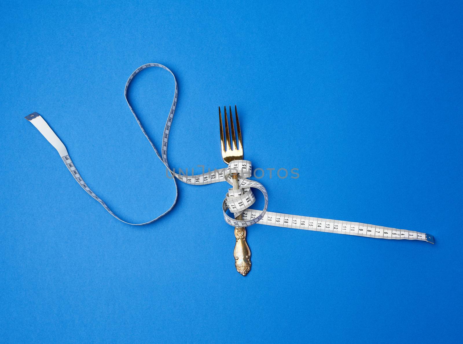 iron fork  wrapped in a measuring tape on a blue background, top view