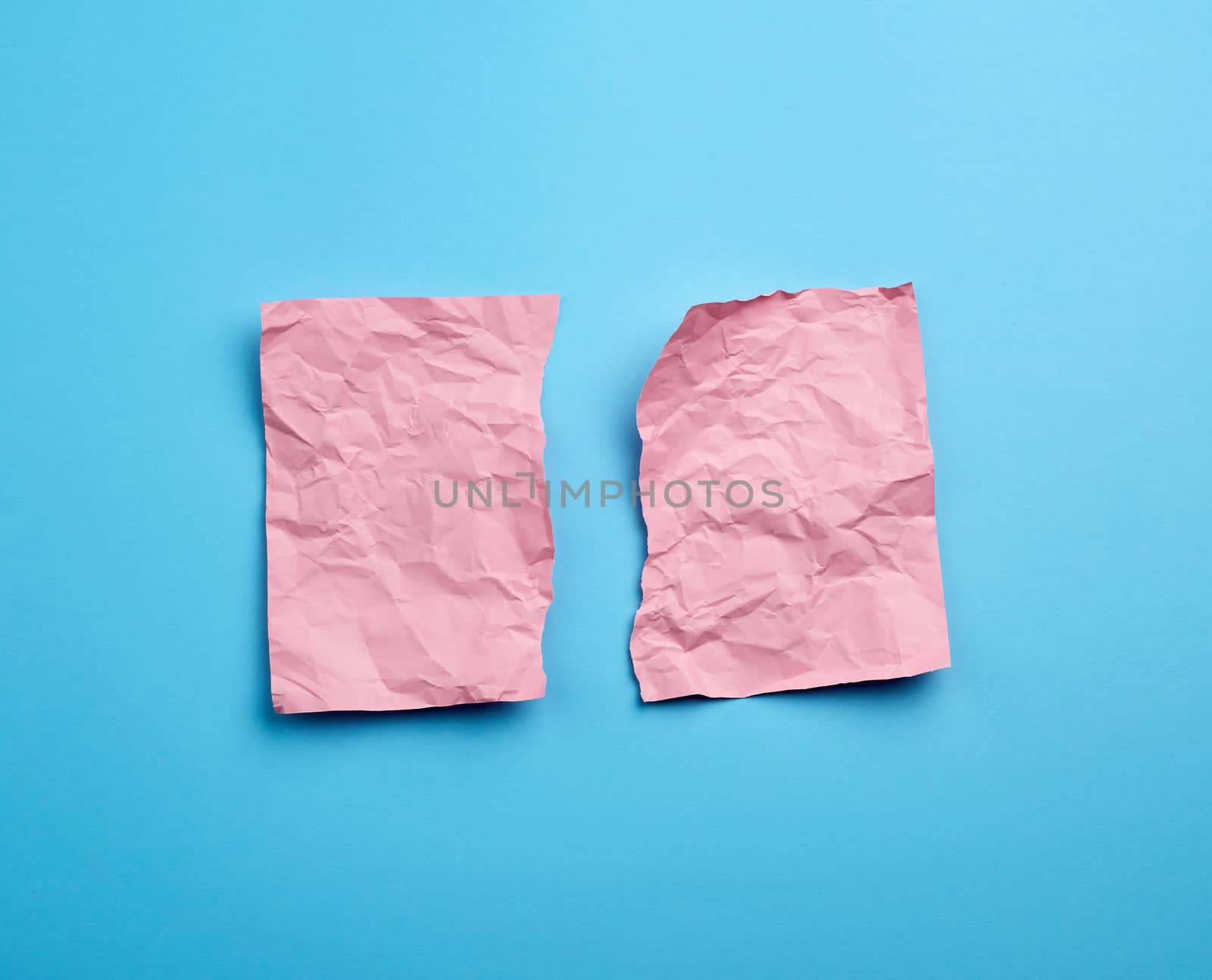crumpled pink sheet of paper torn in two on a blue background. Paper piece torn edge.