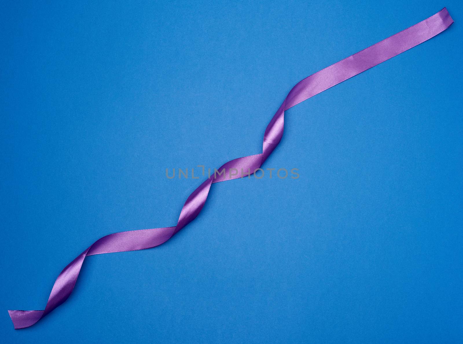 purple silk thin ribbon twisted on a blue background, trendy color, top view