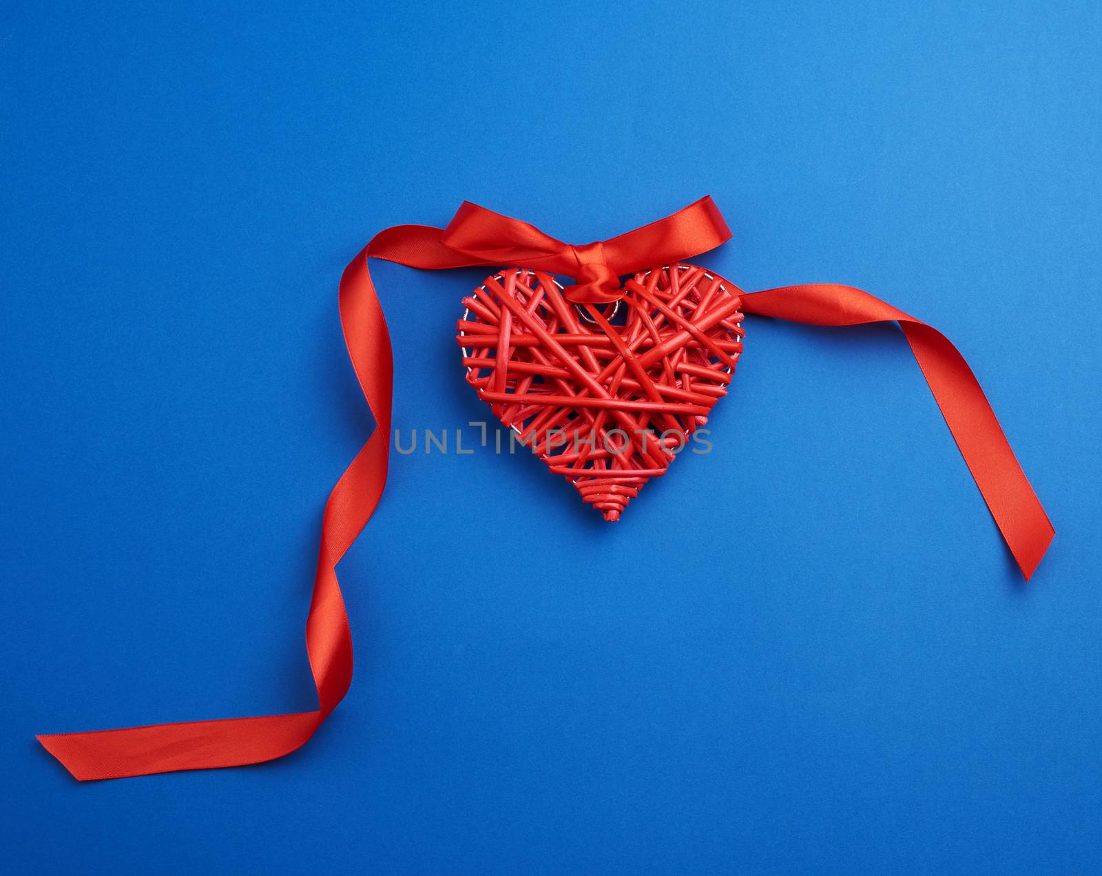 red wicker decorative heart hanging on silk ribbon, blue festive background for Valentine's day