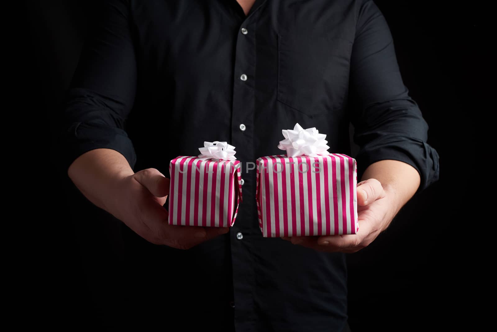 adult man in a black shirt holds in his hand a stack of paper-wrapped gifts, concept of holiday greetings, low key