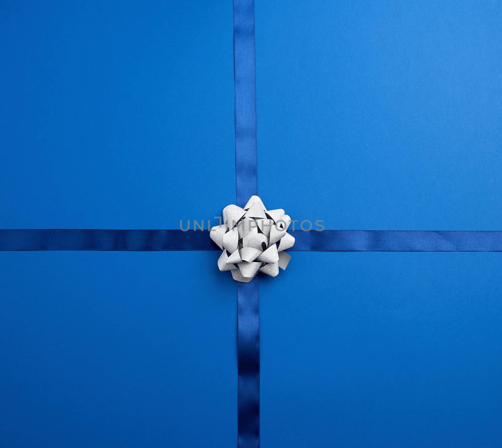 blue silk ribbon crossed on a dark blue background, in the middle a silver bow, imitation of tying a gift, top view
