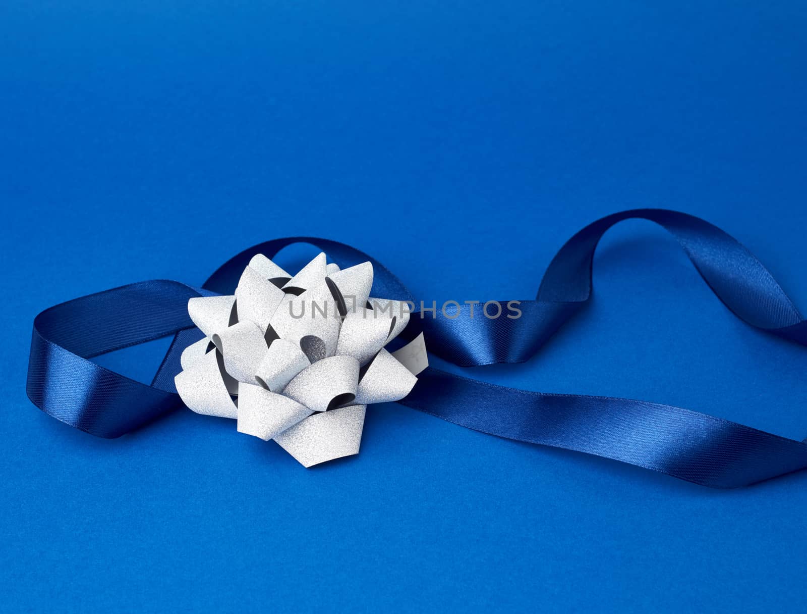 blue silk thin ribbon twisted and gray shiny bow on a blue background, trendy classic color, close up