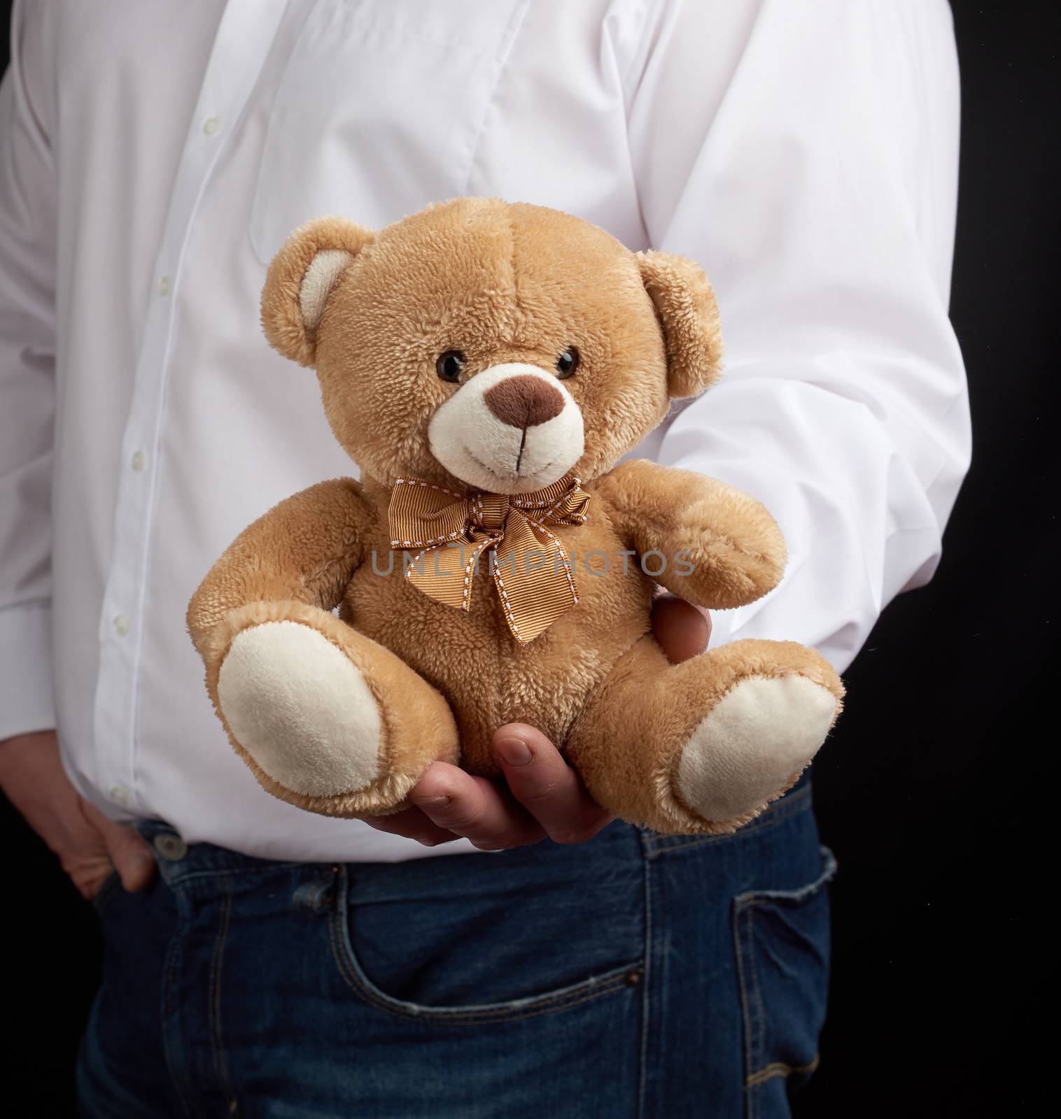 adult man in a white shirt holds a brown teddy bear on a dark background, close up