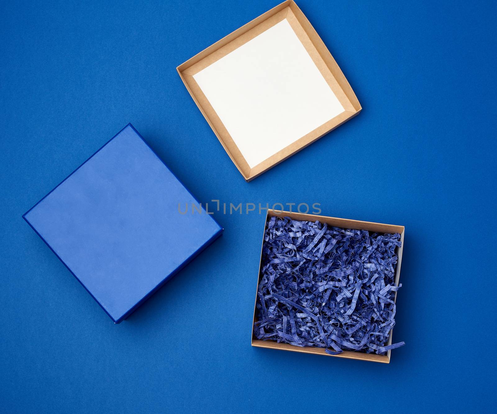 open brown square cardboard empty box, item lies on a blue classic background color, top view