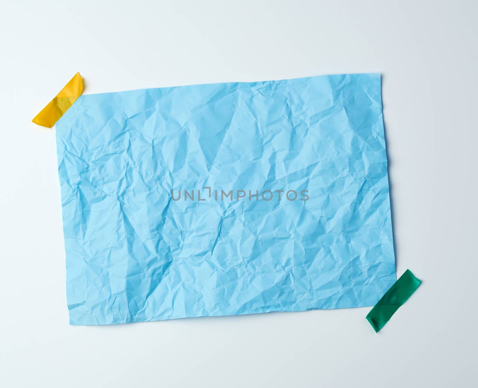 blue crumpled sheet of paper glued with adhesive tape on a white background, place for text