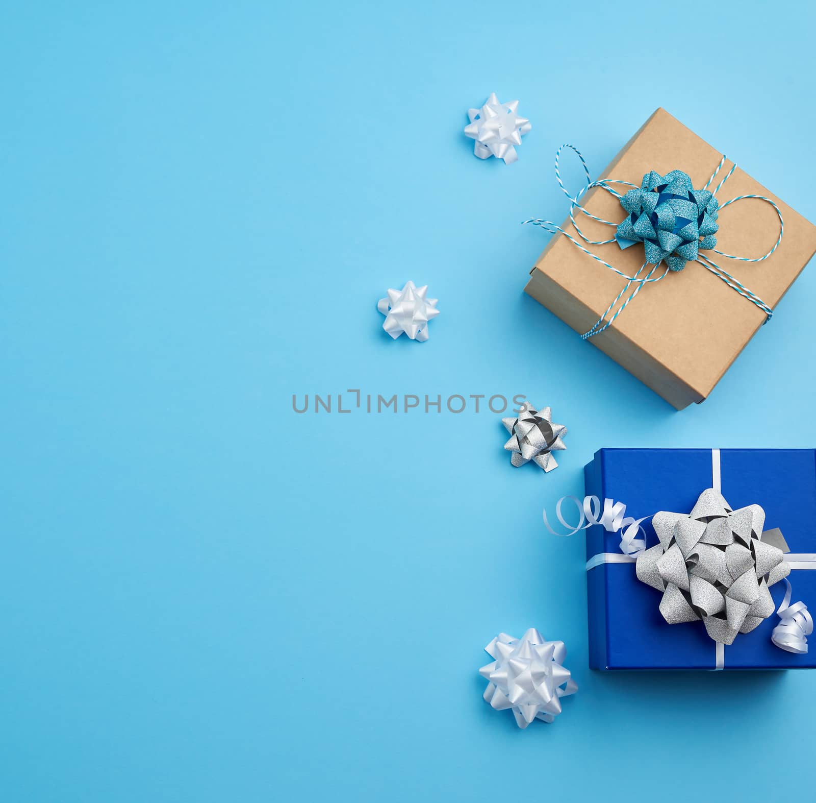 two square gift boxes decorated with ribbons and bows on a blue background, top view, place for text