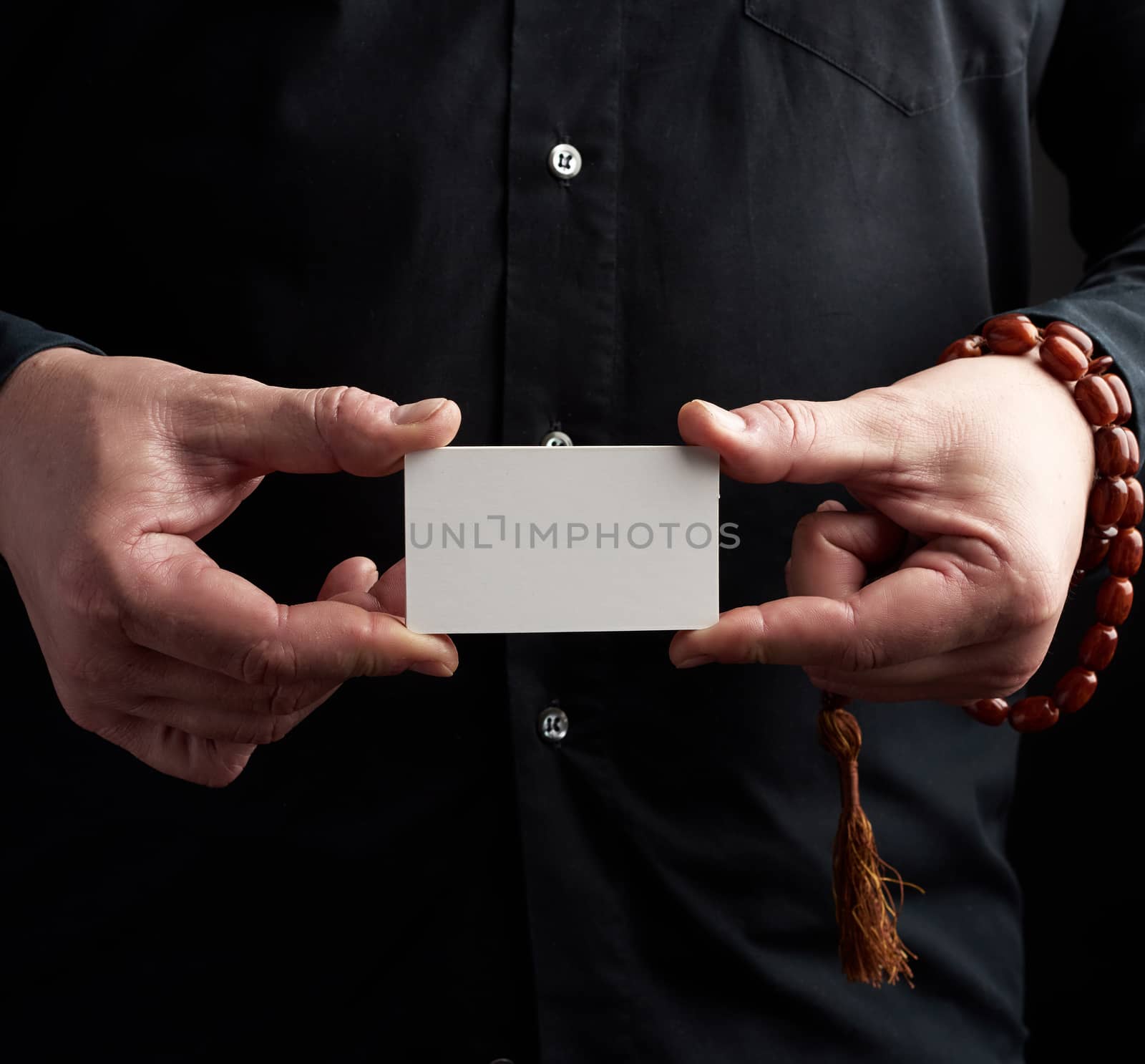 two male hands holding a rectangular blank white paper business card, a man wearing a black shirt, place for inscription