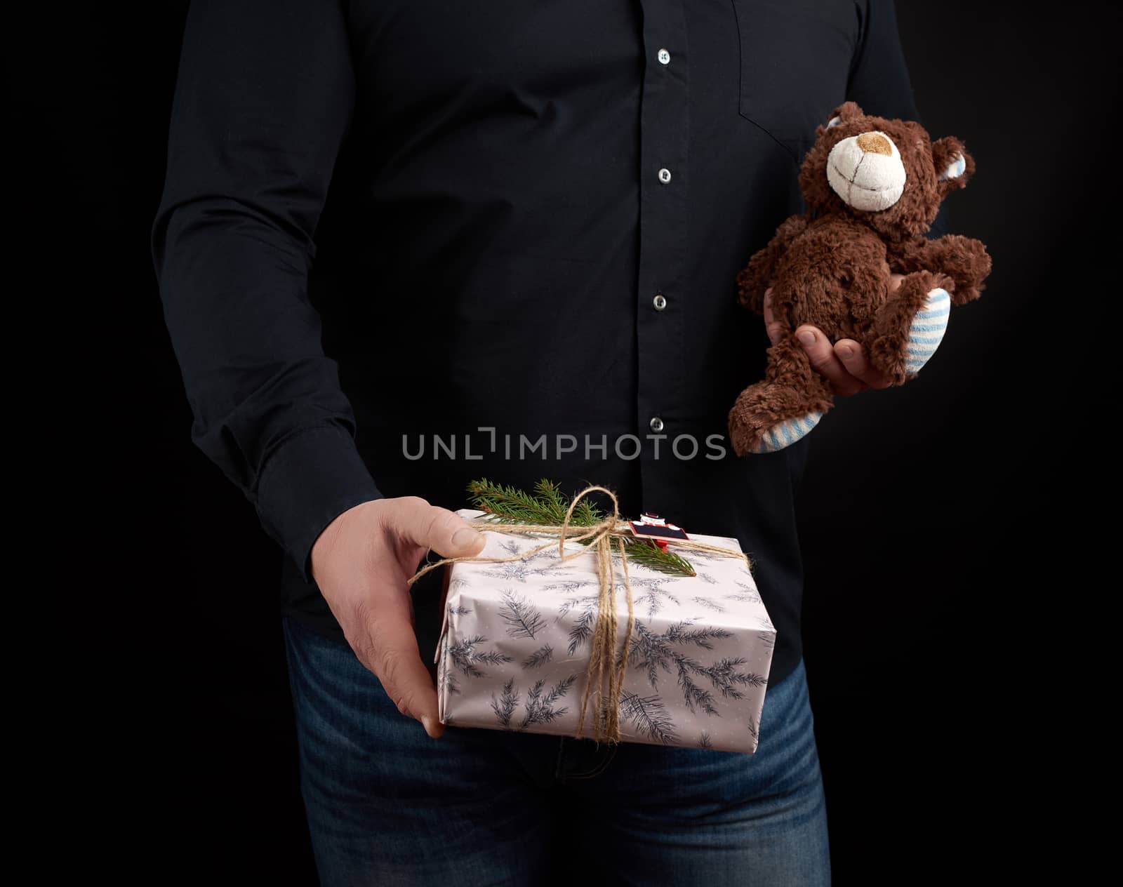 adult man in a black shirt holds a square box and brown teddy bear, concept of congratulations on Valentine's Day on February 14, low key 