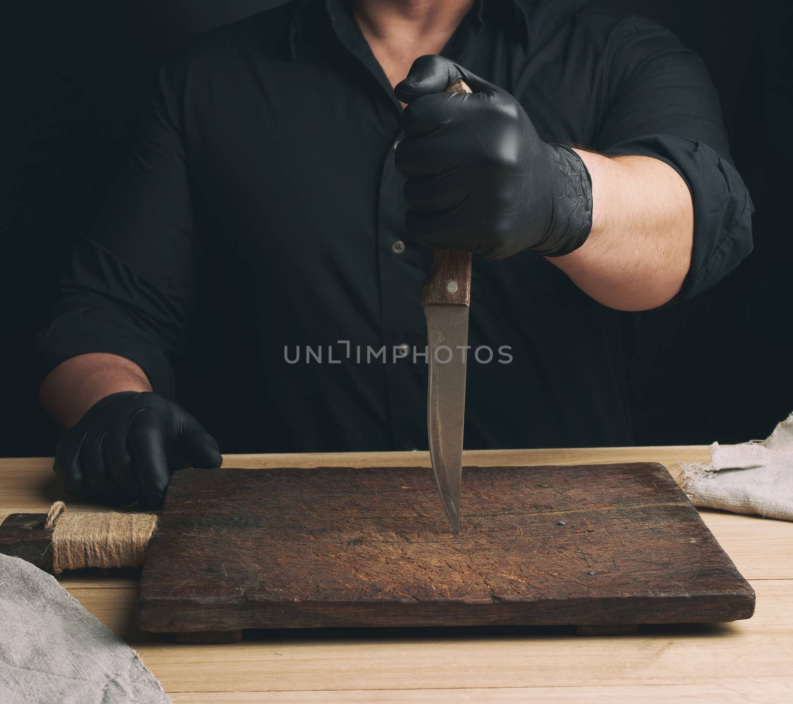 chef in a black shirt and black latex gloves holds a large kitchen knife for cutting meat, low key