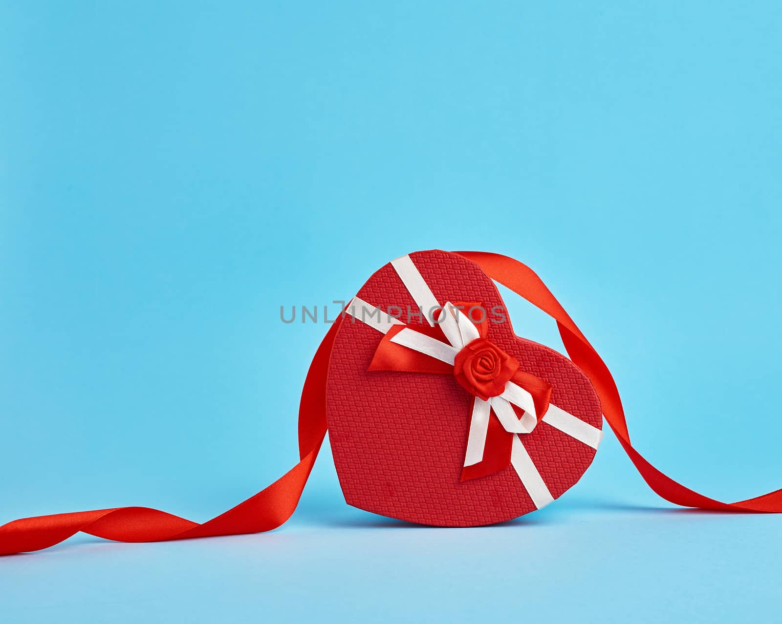 closed red heart-shaped gift box with a red bow on a blue background, top view, festive backdrop. Valentine gift