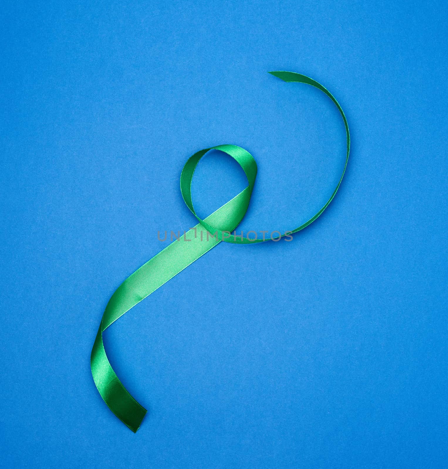 green silk thin ribbon twisted on a blue background, top view