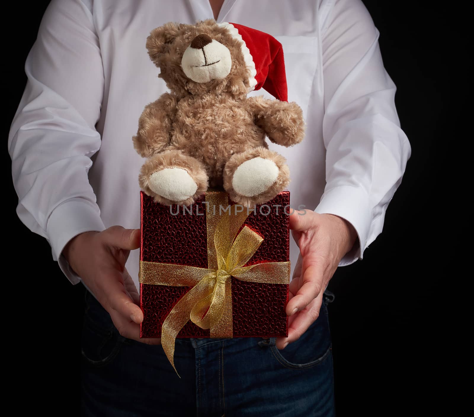 adult man in a white shirt holds a red square box tied with a golden ribbon and brown teddy bear, Merry Christmas and Happy New Year greetings concept