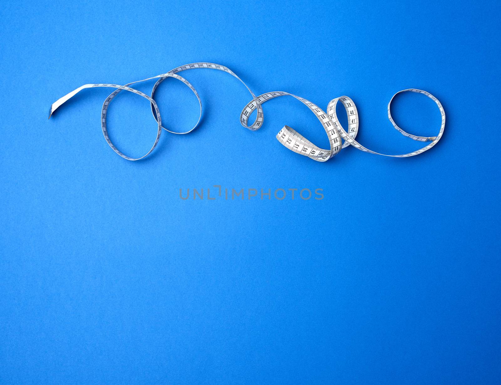 twisted measuring tape on a blue background, copy space