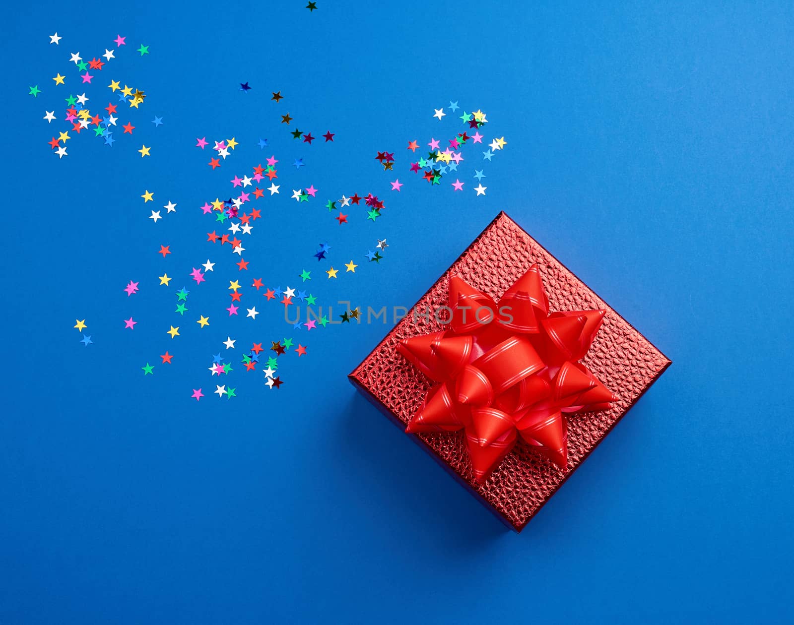 square red shiny box with a bow and multicolored sparkles on a blue background, top view. Valentine gift. Gift symbol. Christmas gift box.