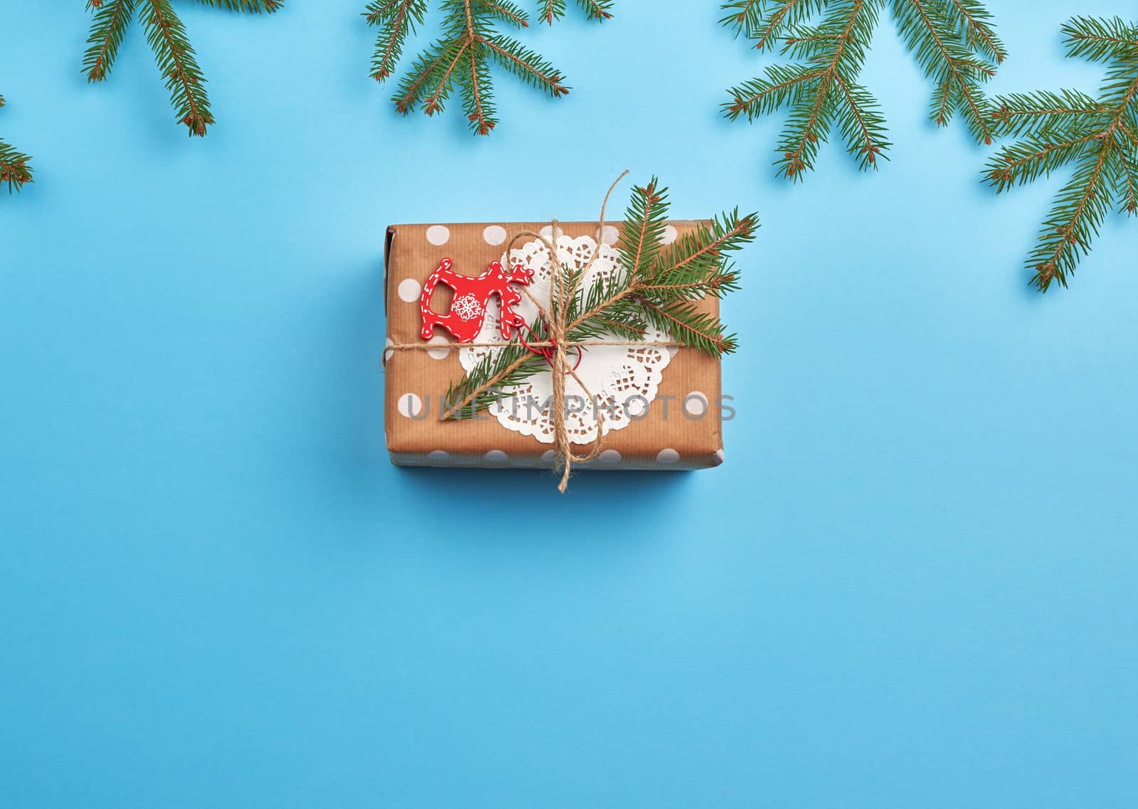 gift wrapped in brown craft paper and tied with a brown rope, decor from a green spruce branch on a blue background, top view