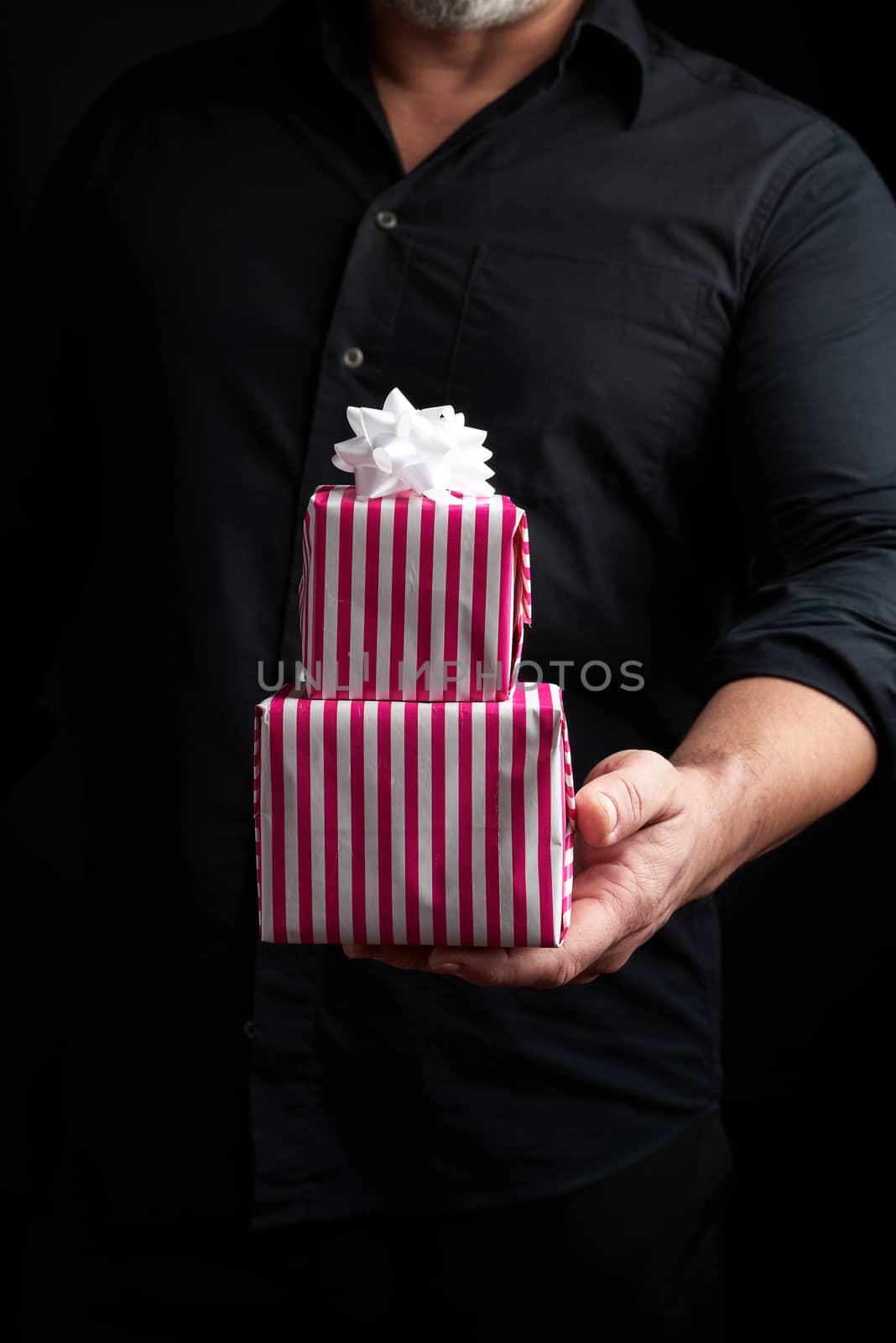 adult man in a black shirt holds in his hand a stack of paper-wrapped gifts, concept of holiday greetings, low key