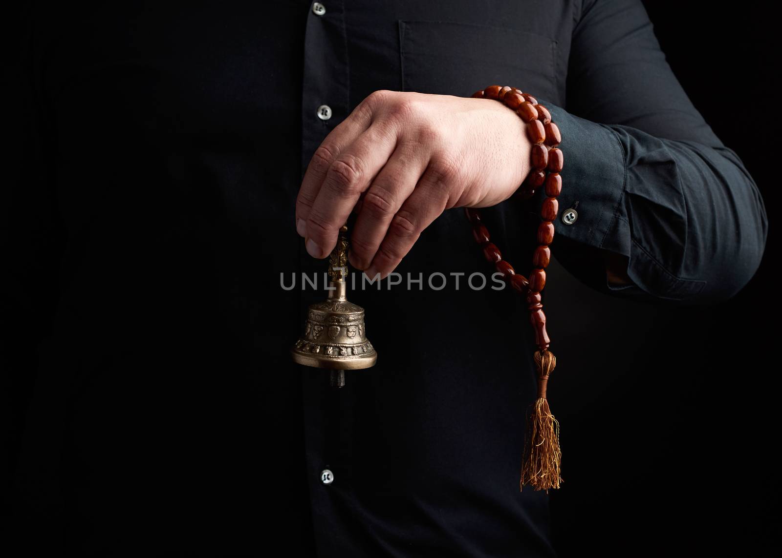 adult man in a black shirt holds a copper Tibetan ritual bell, low key. bell represents the feminine principle of excellence in wisdom.