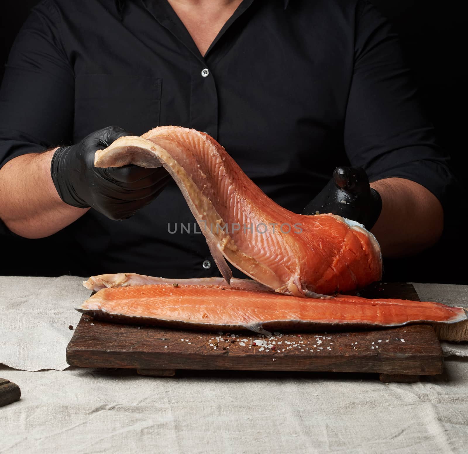 chef in a black shirt and black latex gloves holds a large piece of salmon fish fillet over the table, cooking process, clouse up