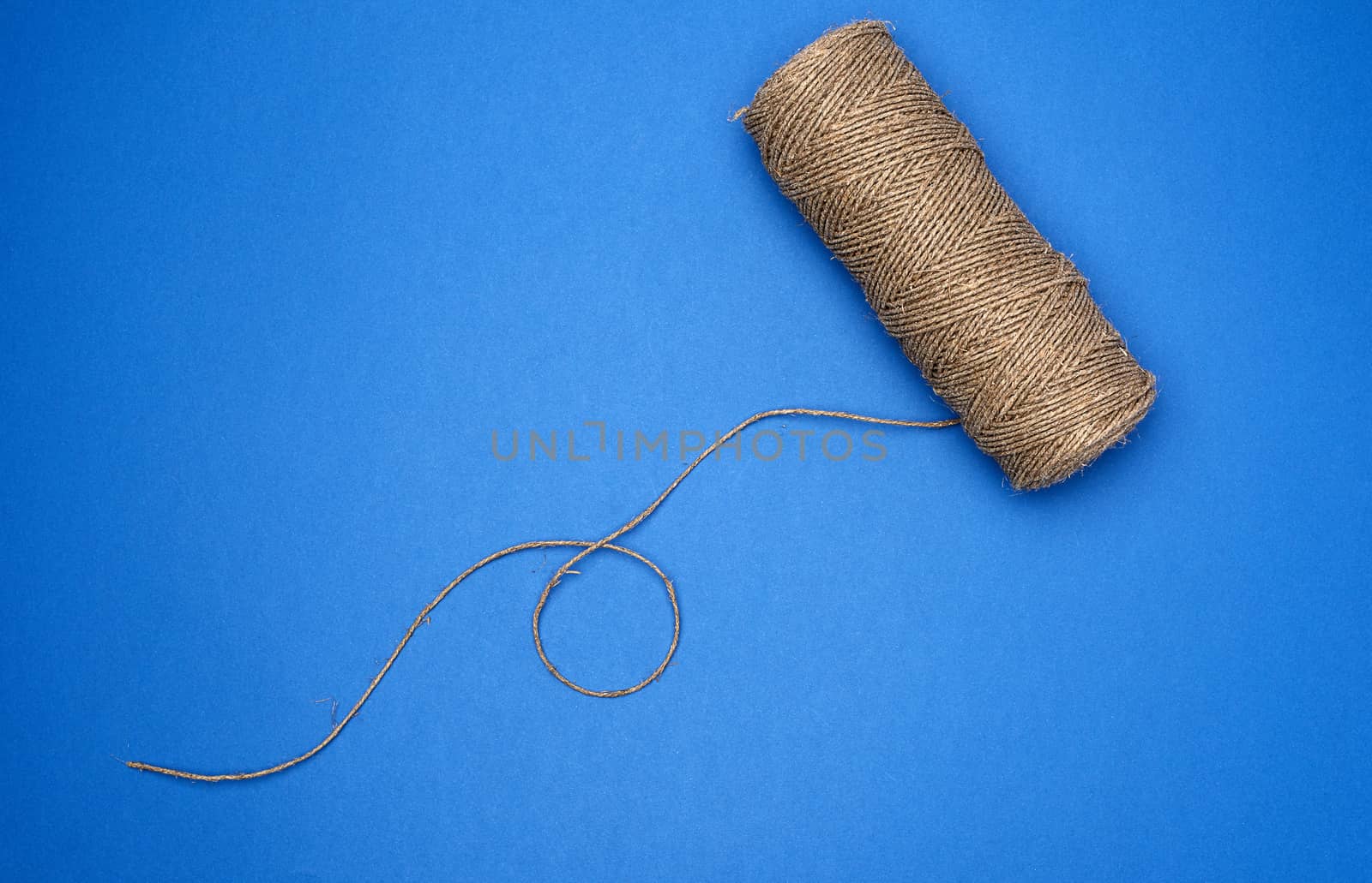 whole coil of twisted brown rope jute tourniquet, eco-friendly packagingm blue background 