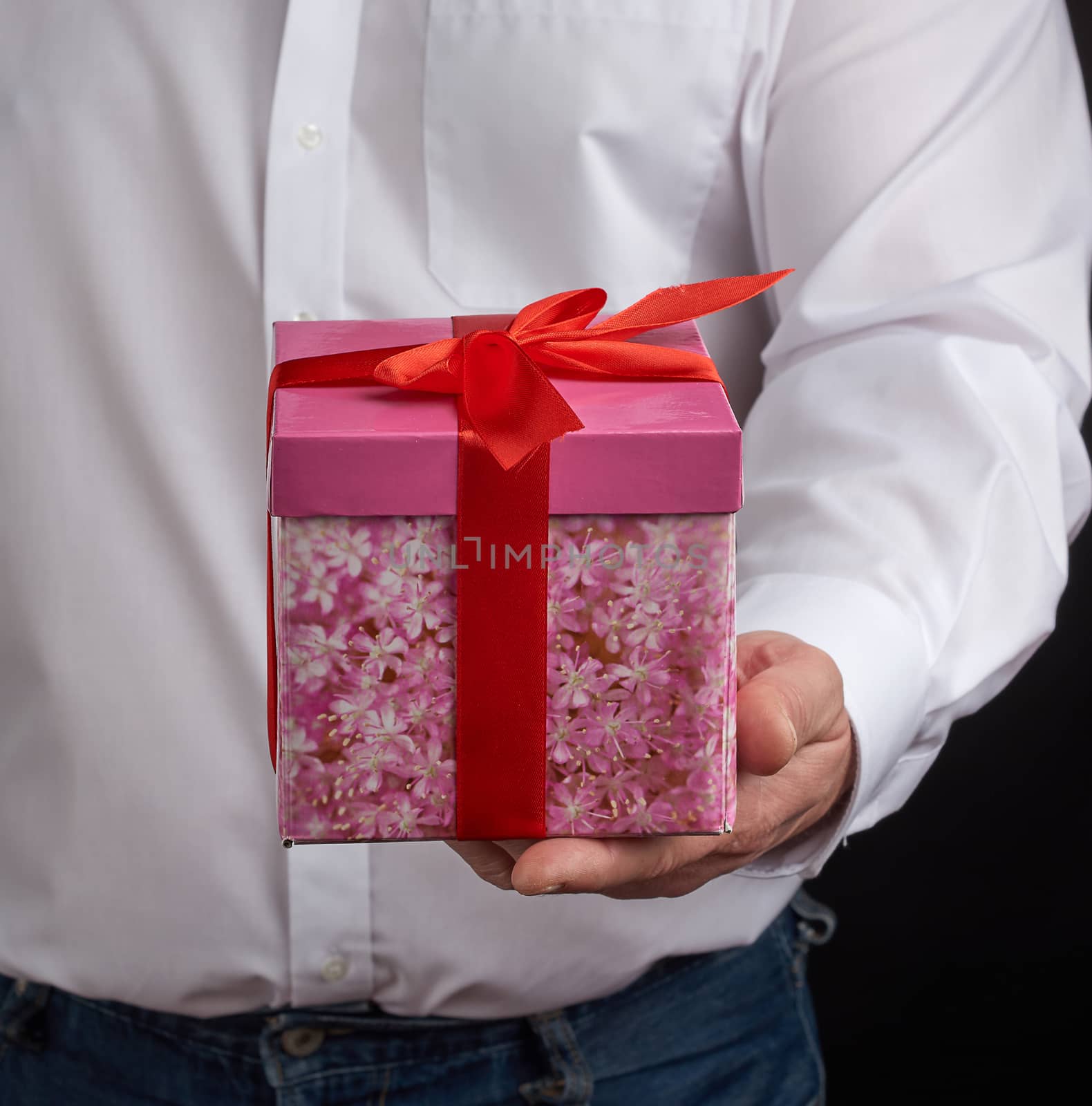 adult man in a white shirt holds a pink gift cardboard box with a bow, concept of a congratulation on the holiday, anniversary, surprise