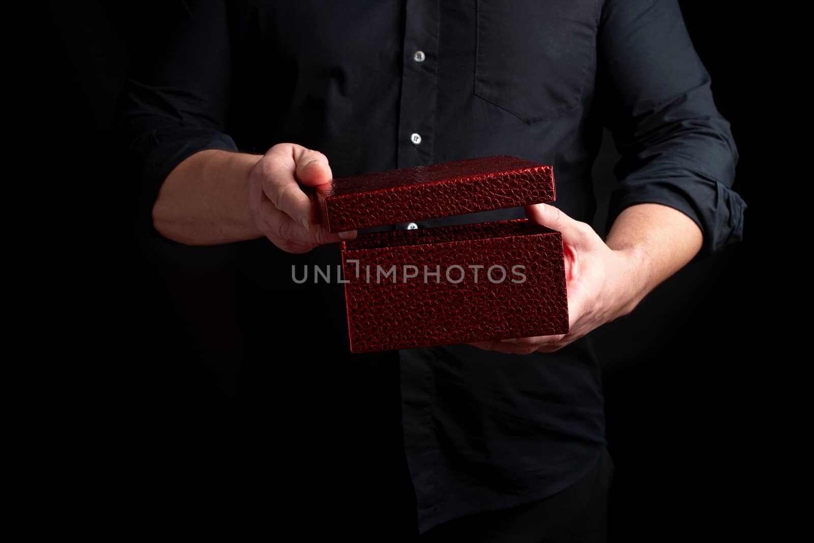 adult man in a black shirt holds a cardboard red gift box and opens the lid, dark background