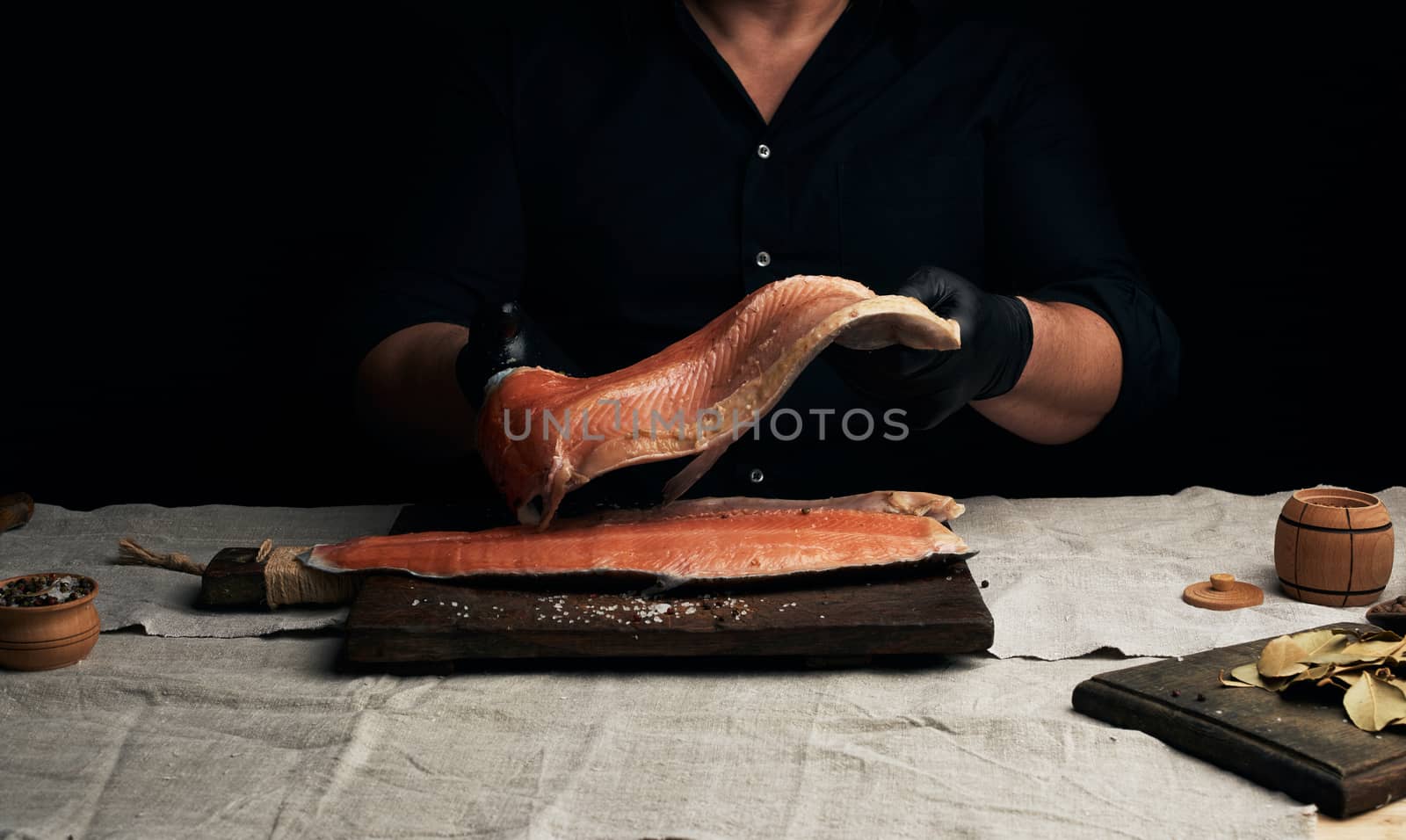 chef in a black shirt and black latex gloves holds a large piece of salmon fish fillet over the table, cooking process, clouse up