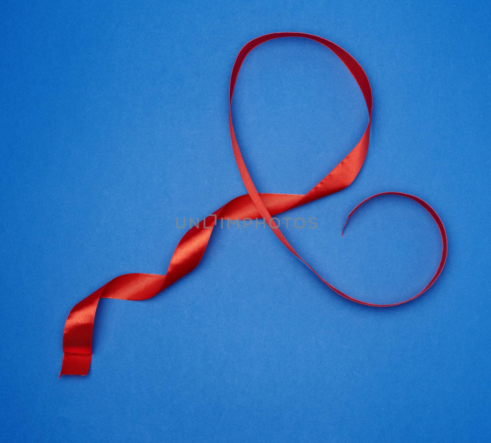red silk thin ribbon twisted on a blue background, trendy classic color, top view
