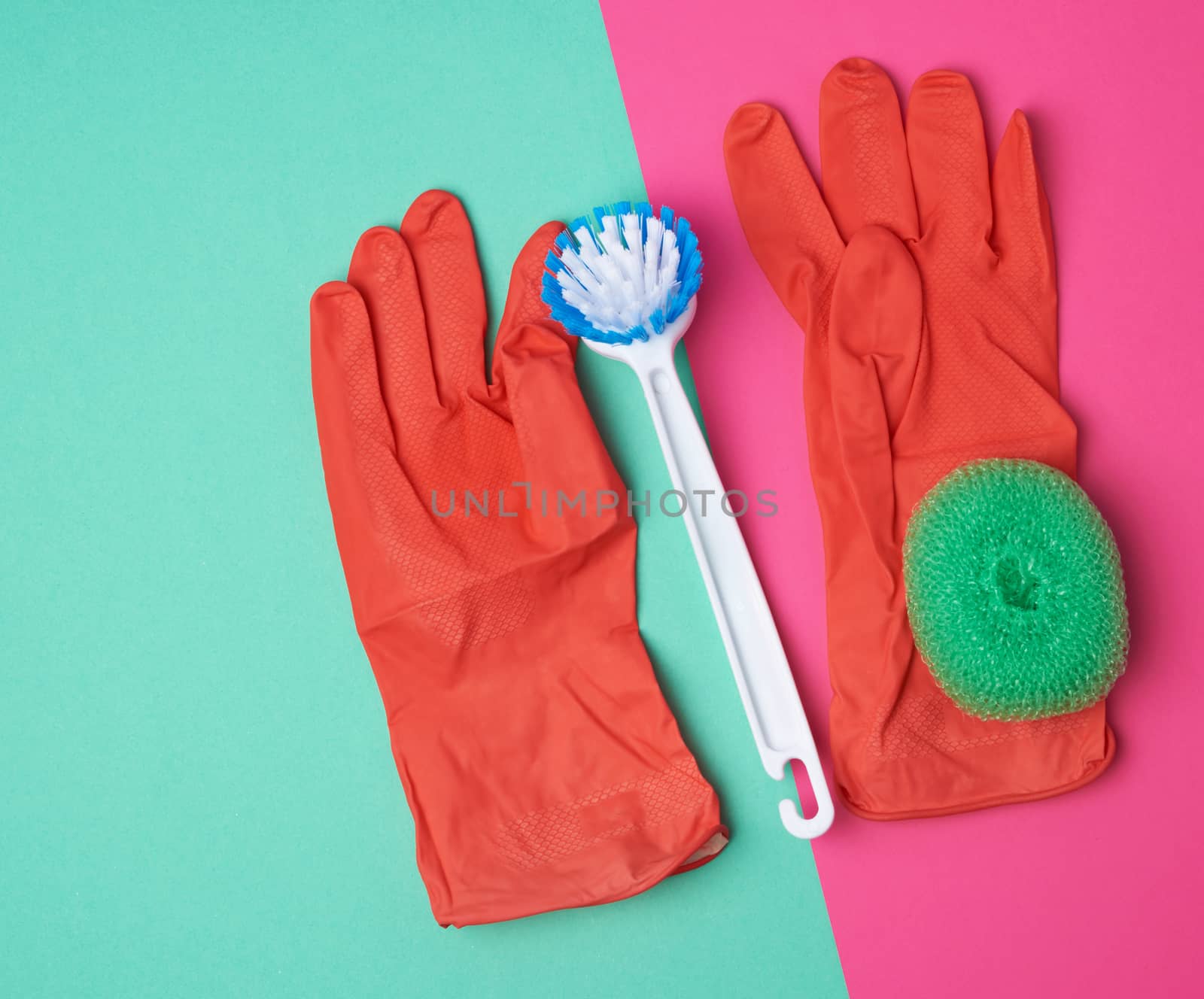 items for home cleaning: red rubber gloves, brush, green sponge for dusting on a pink green background, top view, flat lay