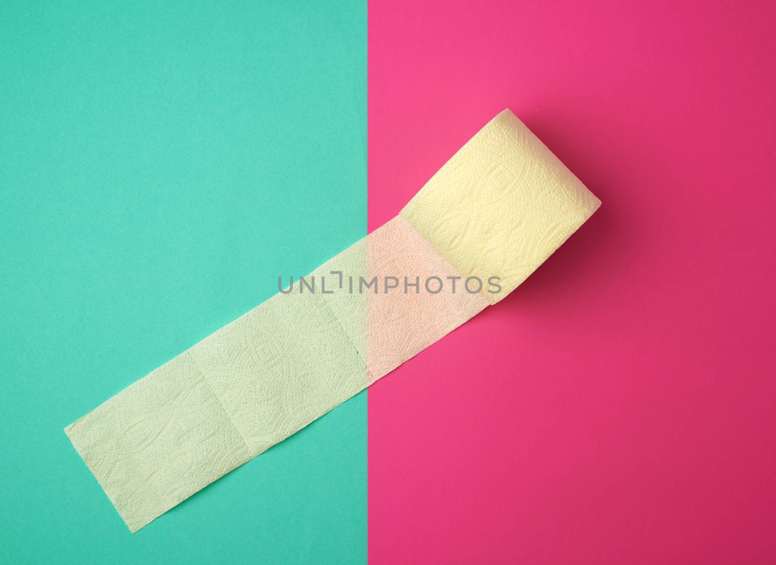 soft yellow toilet paper in a roll on a green-pink background, top view