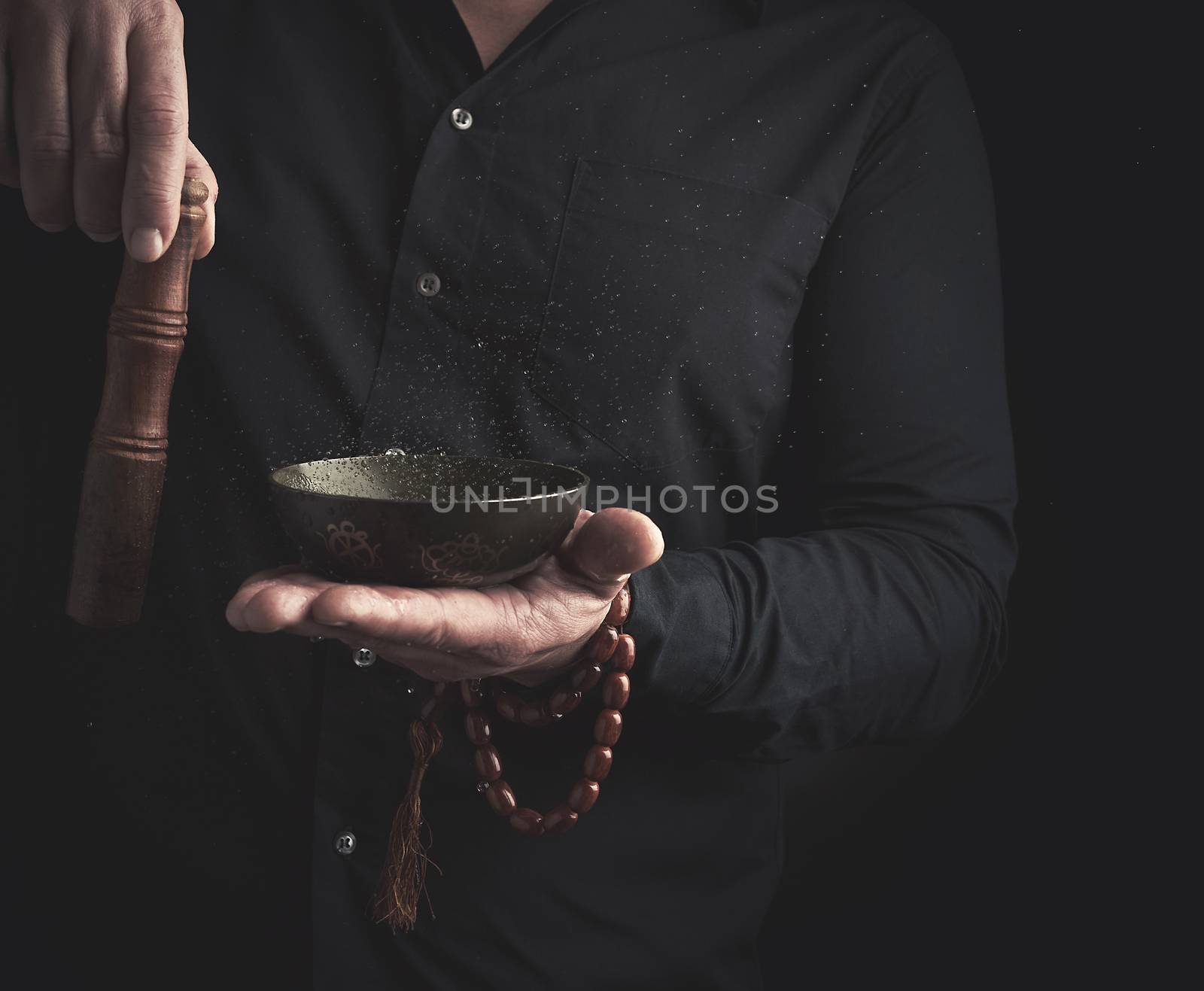 man in a black shirt rotates a wooden stick around a copper Tibetan bowl of water. ritual of meditation, prayers and immersion in a trance. Alternative treatment