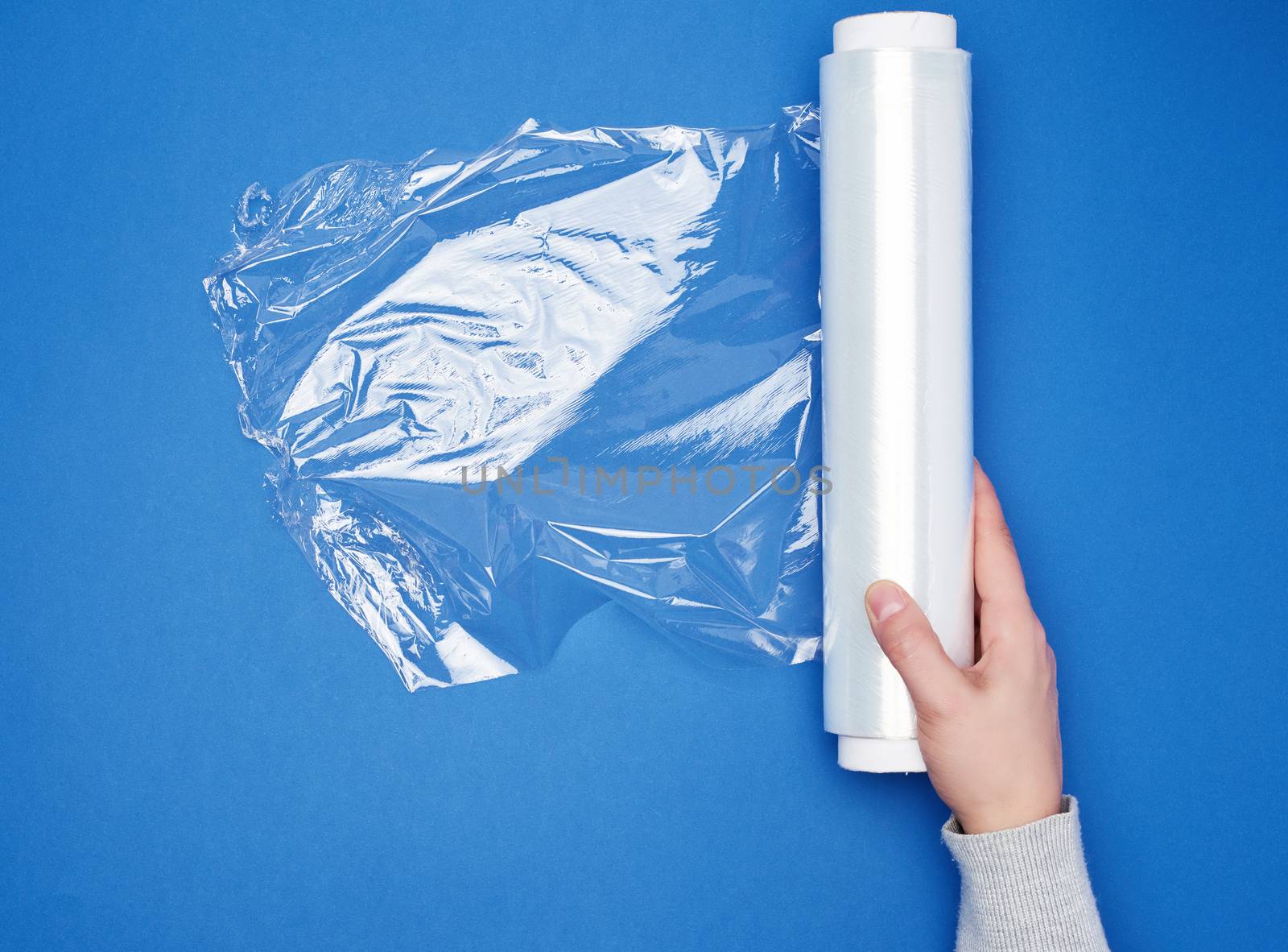 hand hold a large roll of wound white transparent film for wrapping food, top view, blue background 
