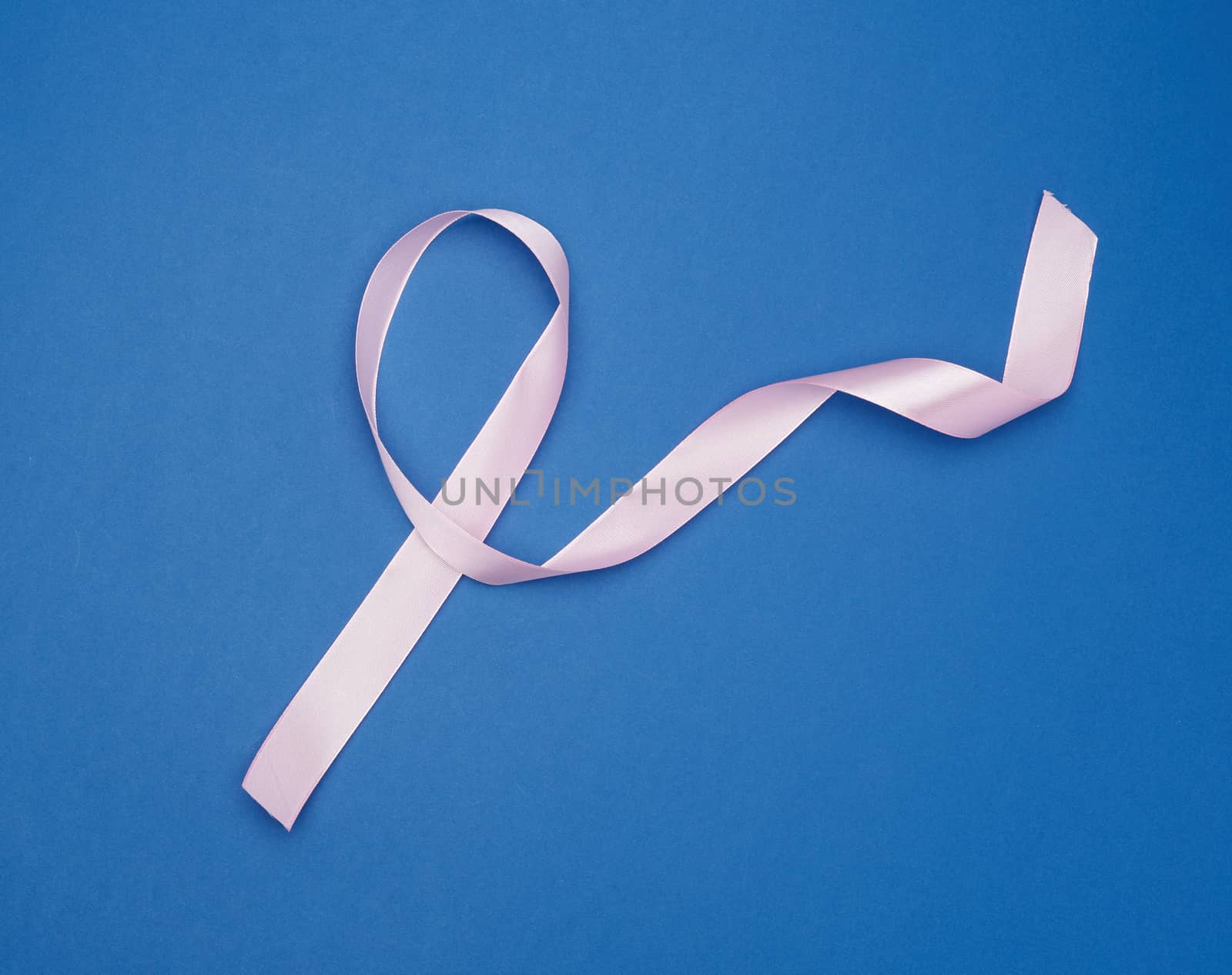 pink silk thin ribbon twisted on a blue background, looped tape with long ends, top view