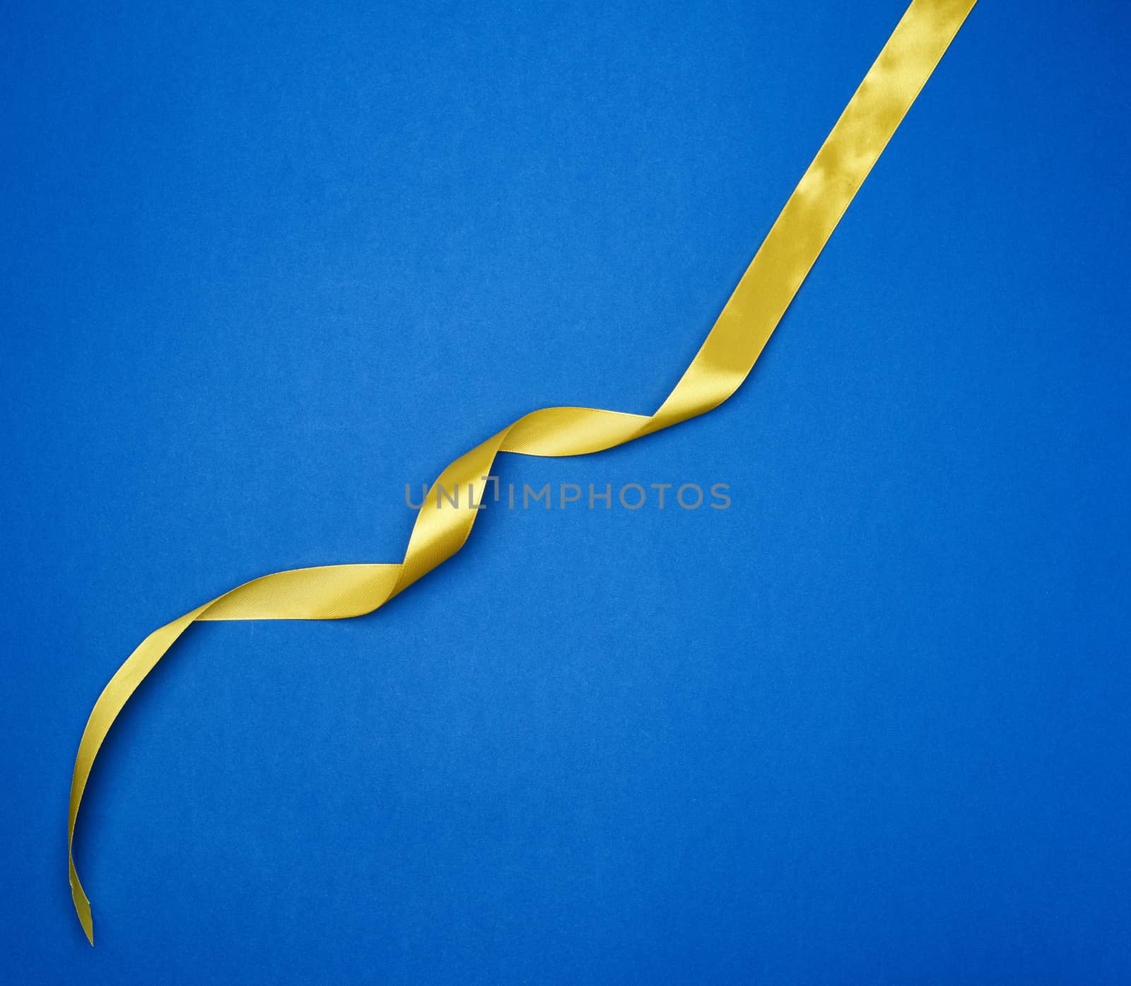 yellow silk thin ribbon twisted on a blue background, trendy classic color, top view