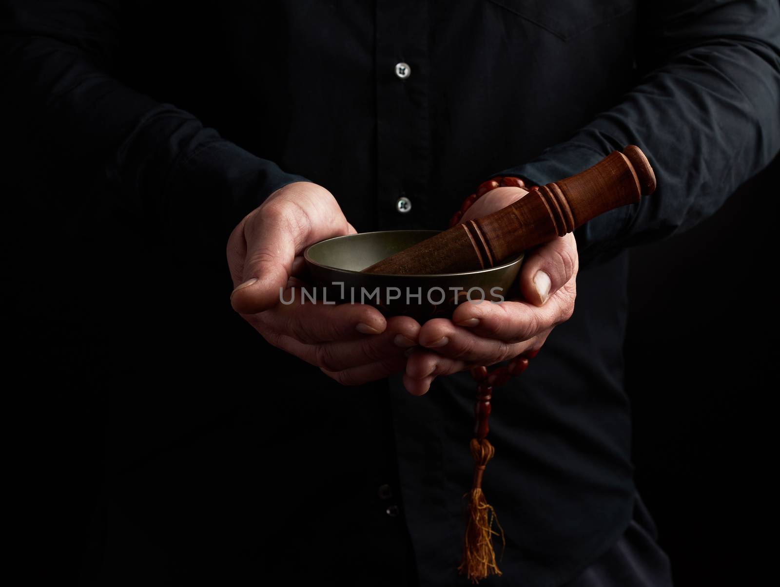 man in a black shirt holds a Tibetan brass singing bowl and a wooden stick, a ritual of meditation, prayers and immersion in a trance. Alternative treatment