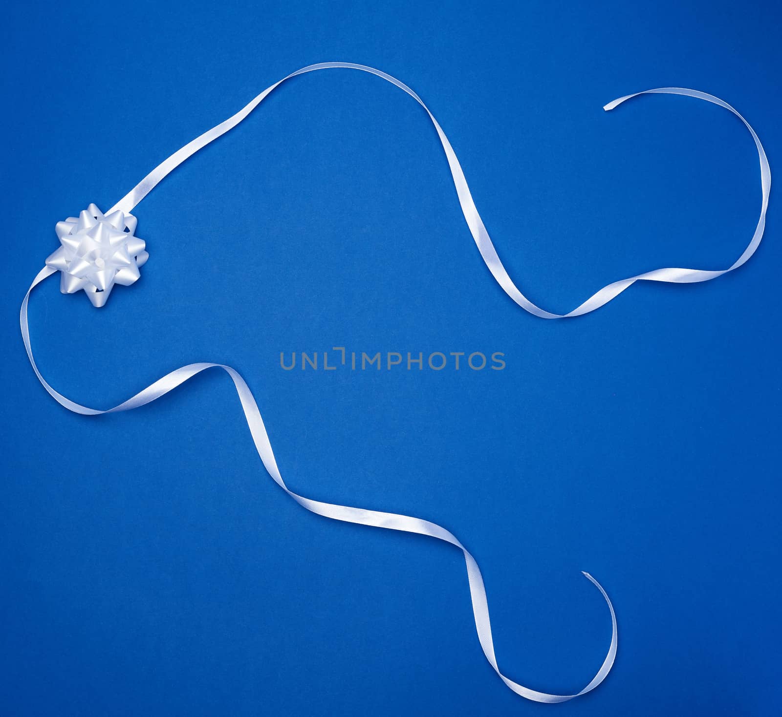 white bow and white silk thin ribbon twisted on a blue background, trendy classic color, top view