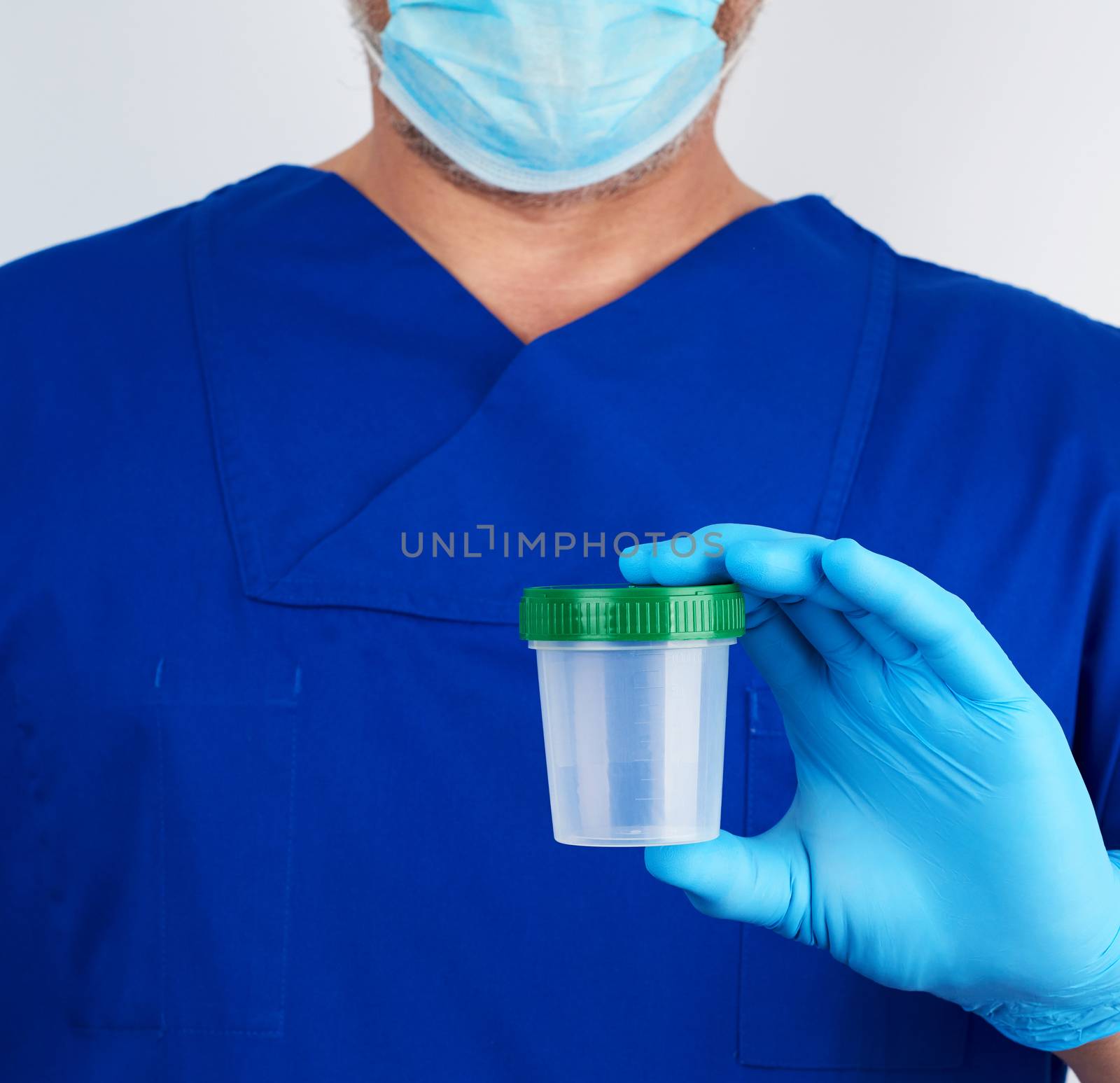 doctor in blue uniform and latex gloves is holding an empty plastic container for taking urine samples, concept of timely diagnosis