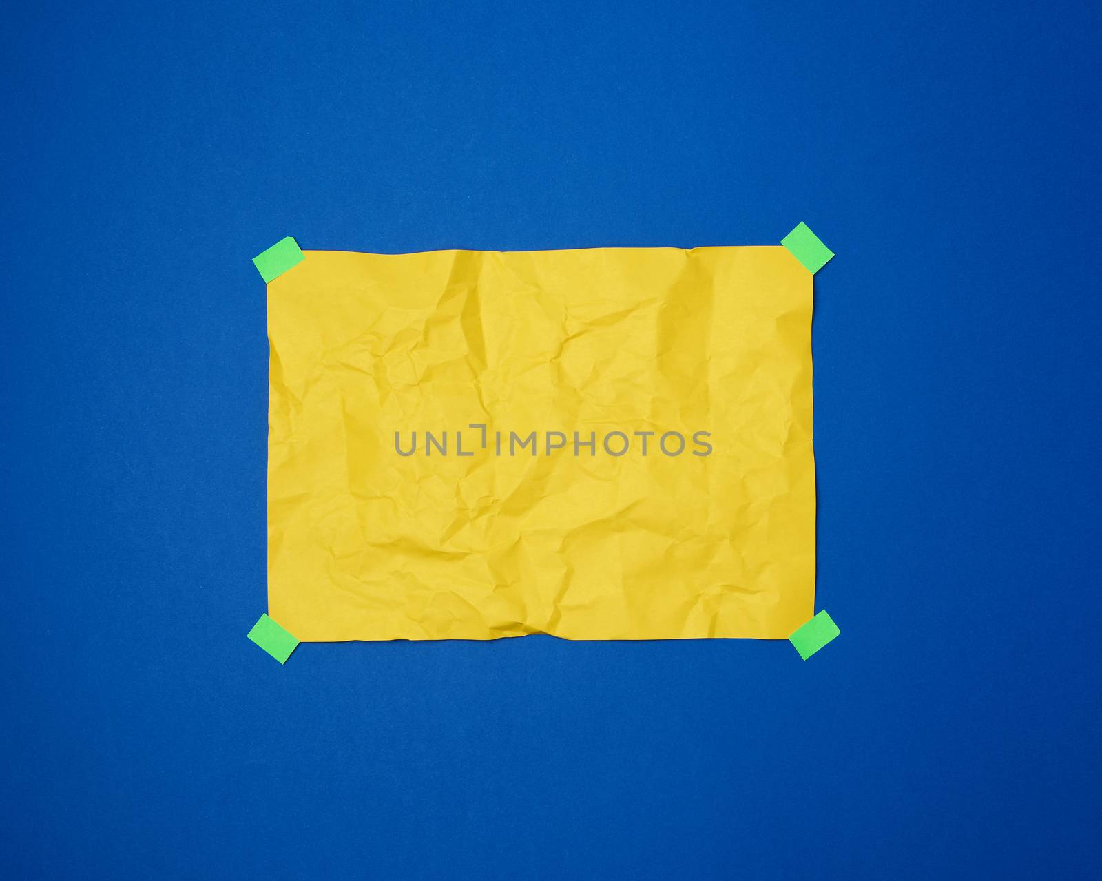 empty yellow crumpled sheet of paper glued with green sticky pieces of paper on a blue background, place for text
