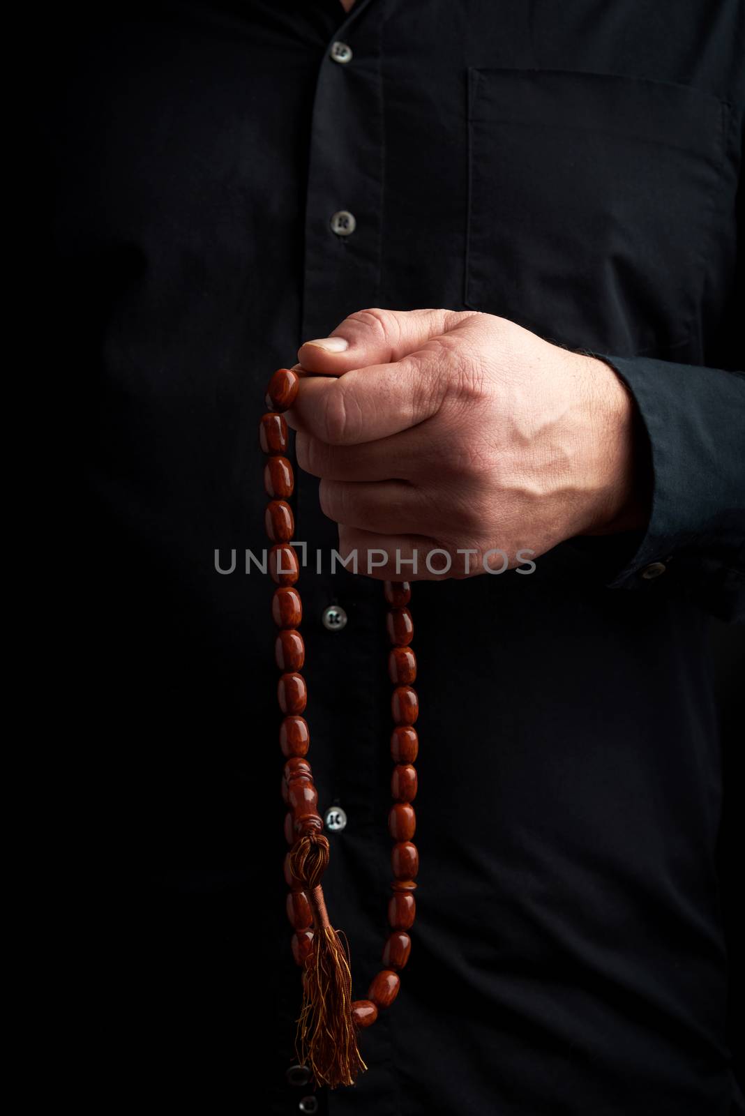 man in a black shirt holds a brown stone rosary in his left hand,  low key. used to count prayers or other ritual actions, to preserve attention and concentration, to set the rhythm