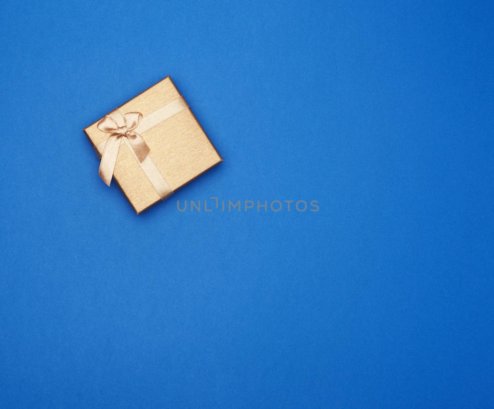 golden cardboard gift square box tied with a ribbon on a dark blue background, top view, trend colors, copy space