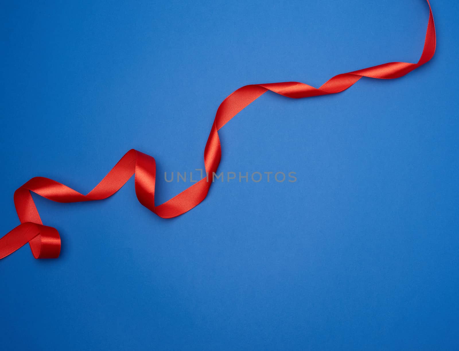red silk thin ribbon twisted on a blue background, trendy classic color, top view