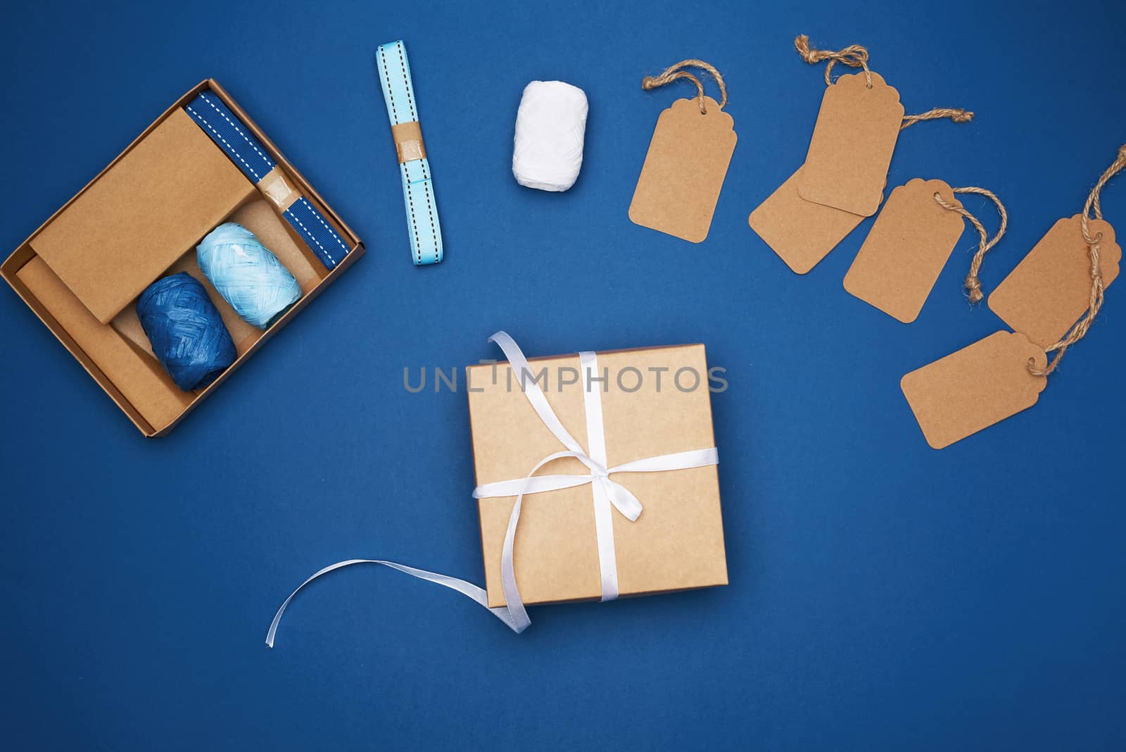 brown cardboard box tied with a white ribbon and a set for packing holiday gifts on a blue background, top view