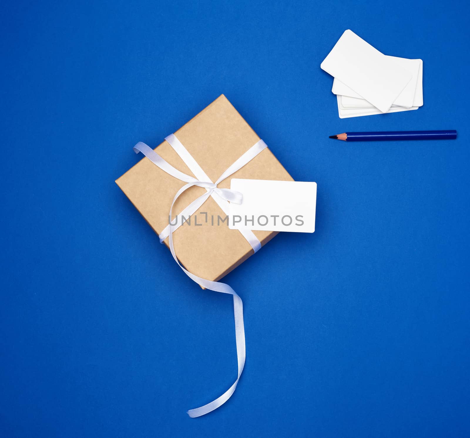 cardboard gift square box tied with a white thin ribbon and white empty card on a dark blue background, top view, trend colors