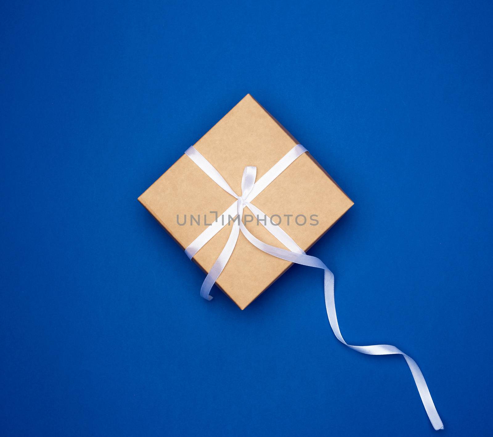 cardboard gift square box tied with a white thin ribbon on a dark blue background, top view, trend colors