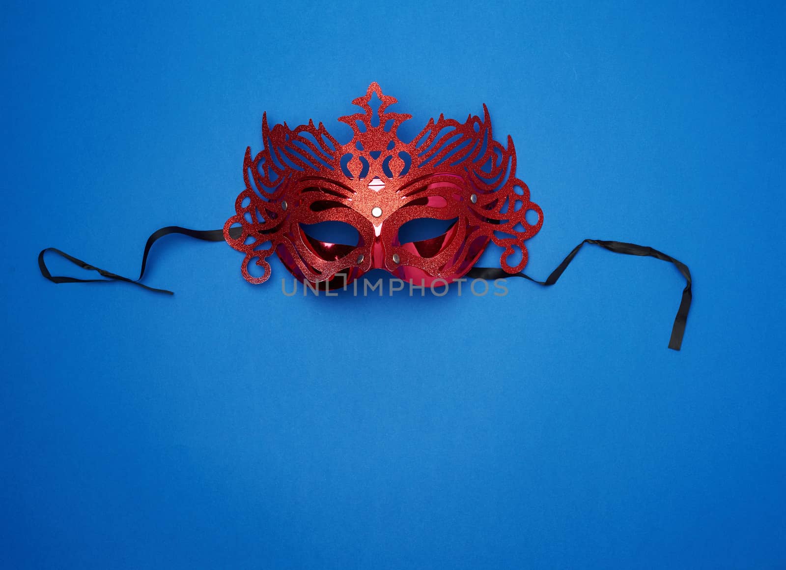 female red carved mask with black ties on a dark blue background, close up
