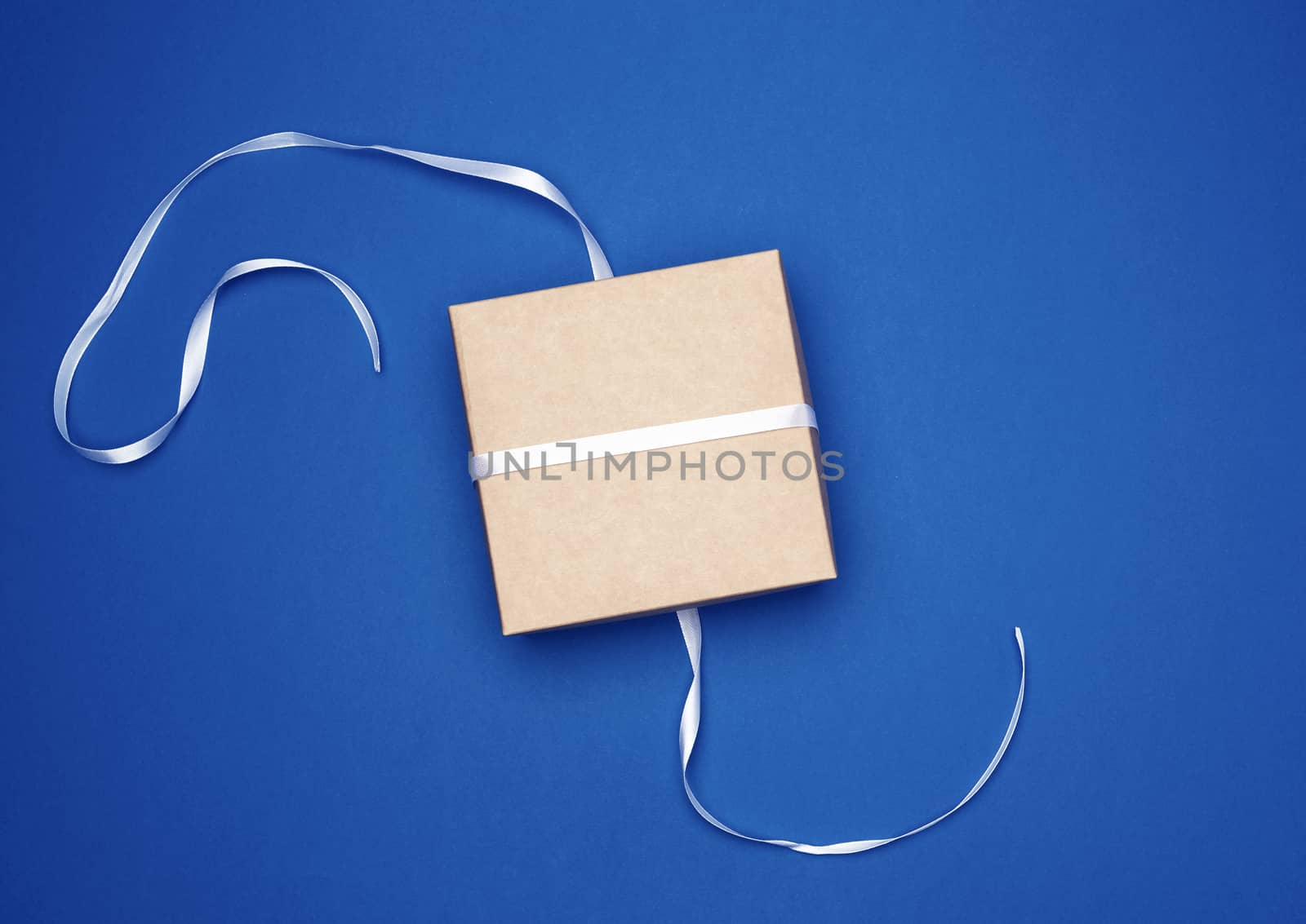 closed blue cardboard gift square box tied white thin ribbon on a dark blue background, top view, trend colors